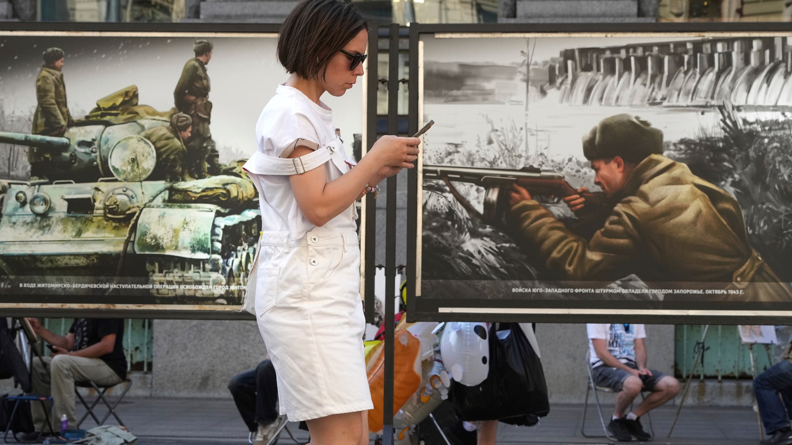 A woman looks at her phone while passing a street exhibition of World War II-era colorized photos in St. Petersburg, Russia, on Monday, July 14, 2025. (AP Photo/Dmitri Lovetsky)