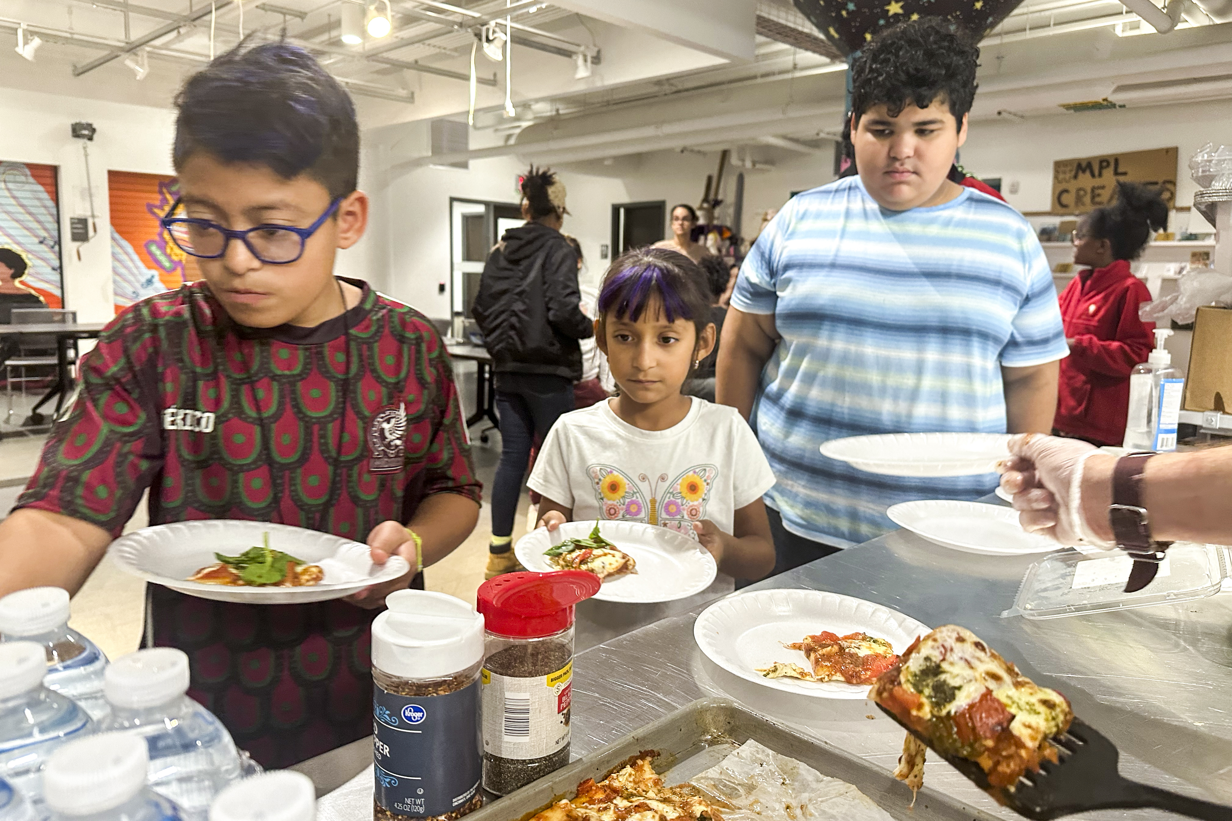 FILE - Attendees of the after school nutrition program, Milwaukee Public Library Snack Hack, line up to get a slice of pizza made from scratch, Nov. 19, 2024, in Milwaukee. (AP Photo/Devi Shastri, File)