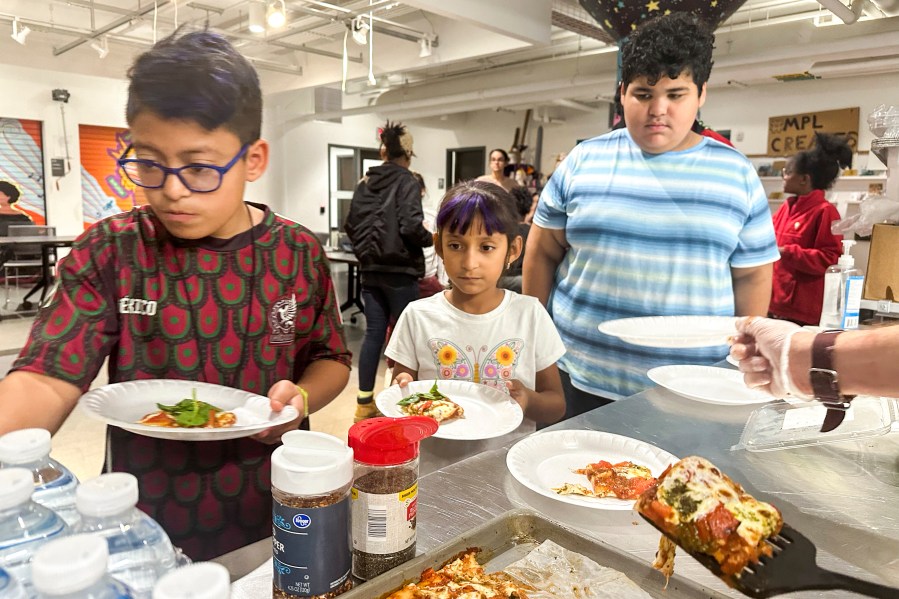 FILE - Attendees of the after school nutrition program, Milwaukee Public Library Snack Hack, line up to get a slice of pizza made from scratch, Nov. 19, 2024, in Milwaukee. (AP Photo/Devi Shastri, File)