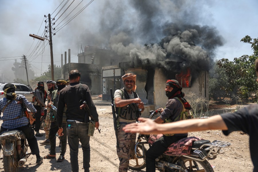 Bedouin fighters gather in front a burned shop at Mazraa village on the outskirts of Sweida city, during clashes between the Bedouin clans and Druze militias, southern Syria, Friday, July 18, 2025. (AP Photo/Ghaith Alsayed)