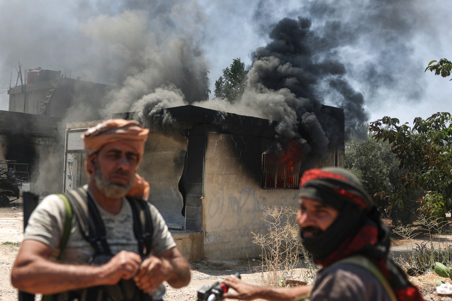 Bedouin fighters stand in front a burned shop at Mazraa village on the outskirts of Sweida city, during clashes between the Bedouin clans and Druze militias, southern Syria, Friday, July 18, 2025. (AP Photo/Ghaith Alsayed)