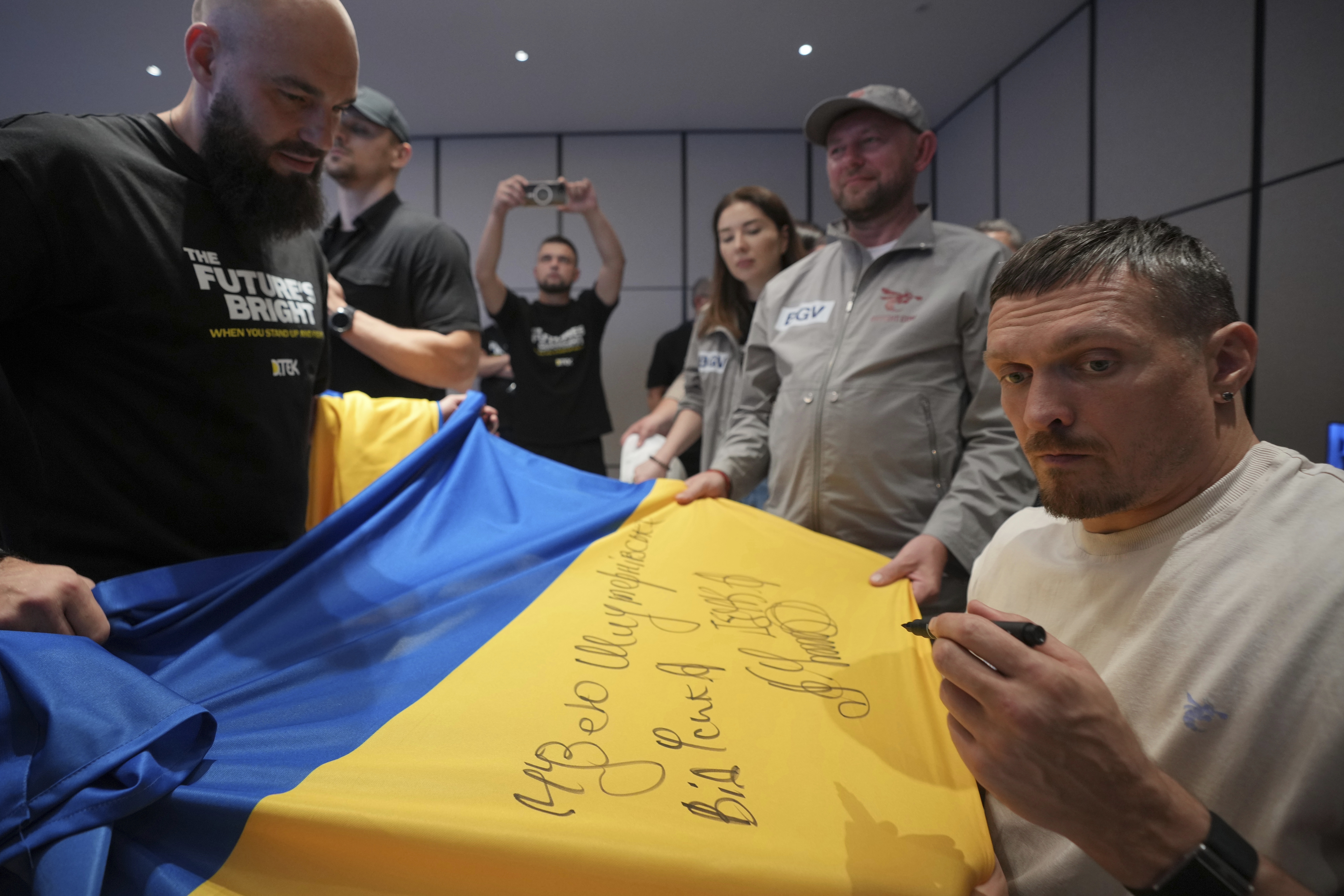 Ukraine's boxer Oleksandr Usyk signs autograph as he meets the Ukrainian war veterans, who are employees of Ukrainian power company DTEK at a hotel in Battersea Park in London, Thursday, July 17, 2025 ahead of the undisputed heavyweight champion boxing fight between Britain's Daniel Dubois and Oleksandr Usyk on Saturday. (AP Photo/Kin Cheung)