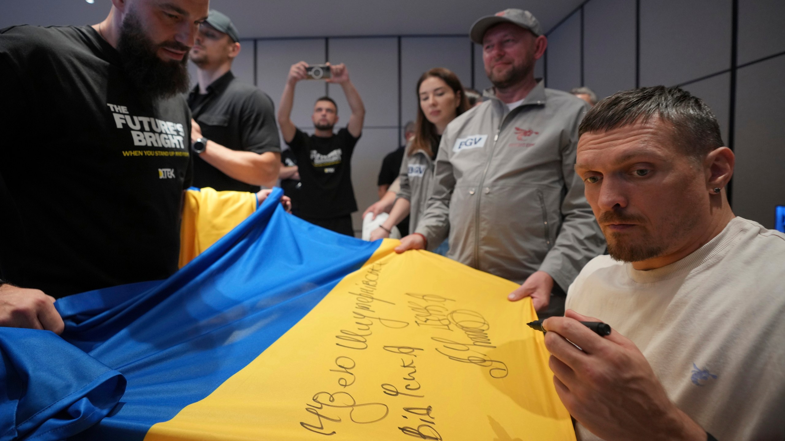 Ukraine's boxer Oleksandr Usyk signs autograph as he meets the Ukrainian war veterans, who are employees of Ukrainian power company DTEK at a hotel in Battersea Park in London, Thursday, July 17, 2025 ahead of the undisputed heavyweight champion boxing fight between Britain's Daniel Dubois and Oleksandr Usyk on Saturday. (AP Photo/Kin Cheung)