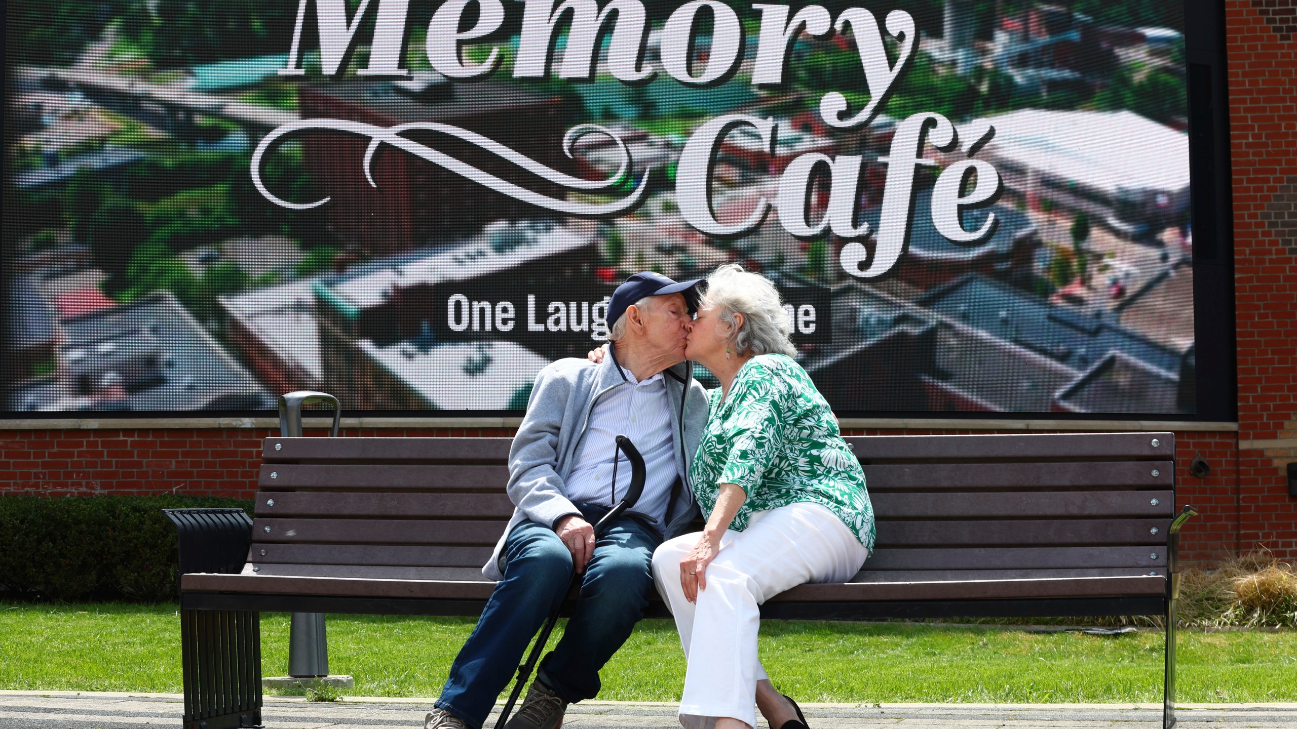 Mario and Gail Cirasunda, of Orchard Park, N.Y., share a kiss on a bench following a Memory Cafe event at the National Comedy Center Monday, May 5, 2025, in Jamestown, N.Y. (AP Photo/Jeffrey T. Barnes)