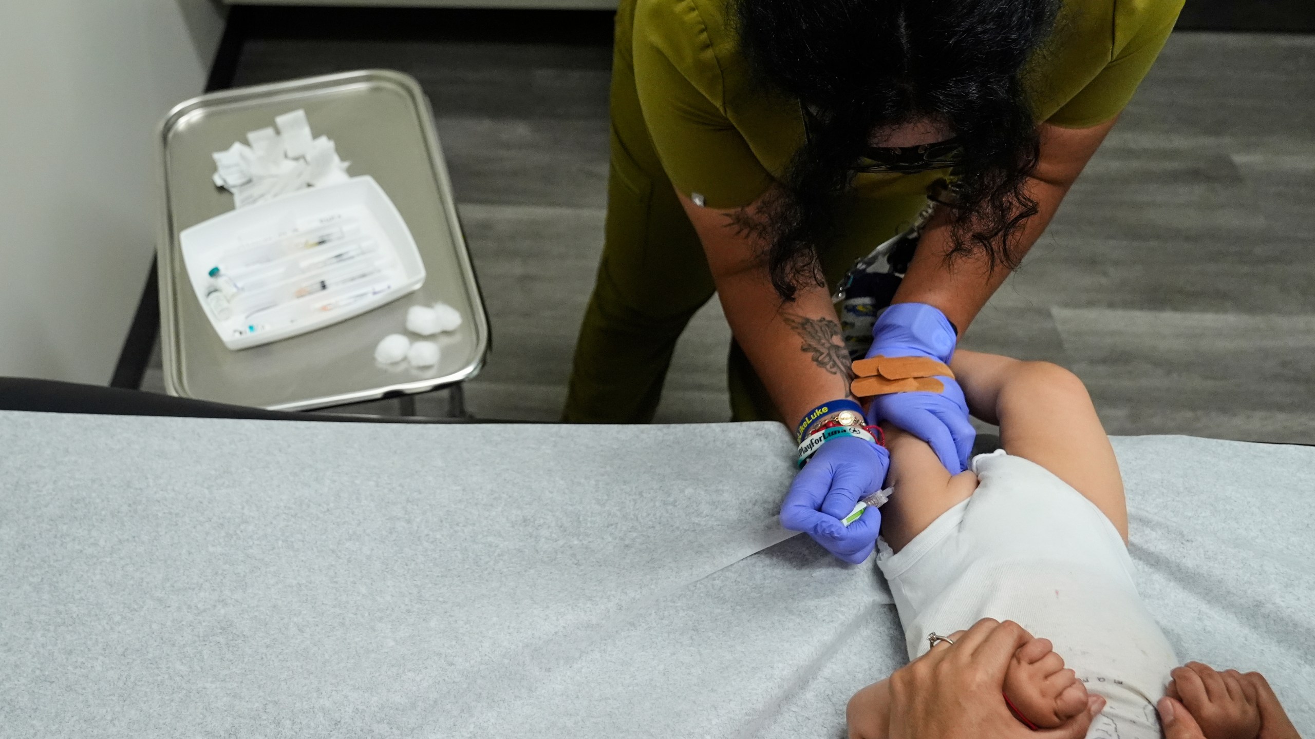 Medical assistant Citlalli Llamas, top, administers a round of vaccines to a 16-month-old boy at a CommuniCARE+OLE clinic Thursday, June 26, 2025, in Davis, Calif. (AP Photo/Godofredo A. Vásquez)