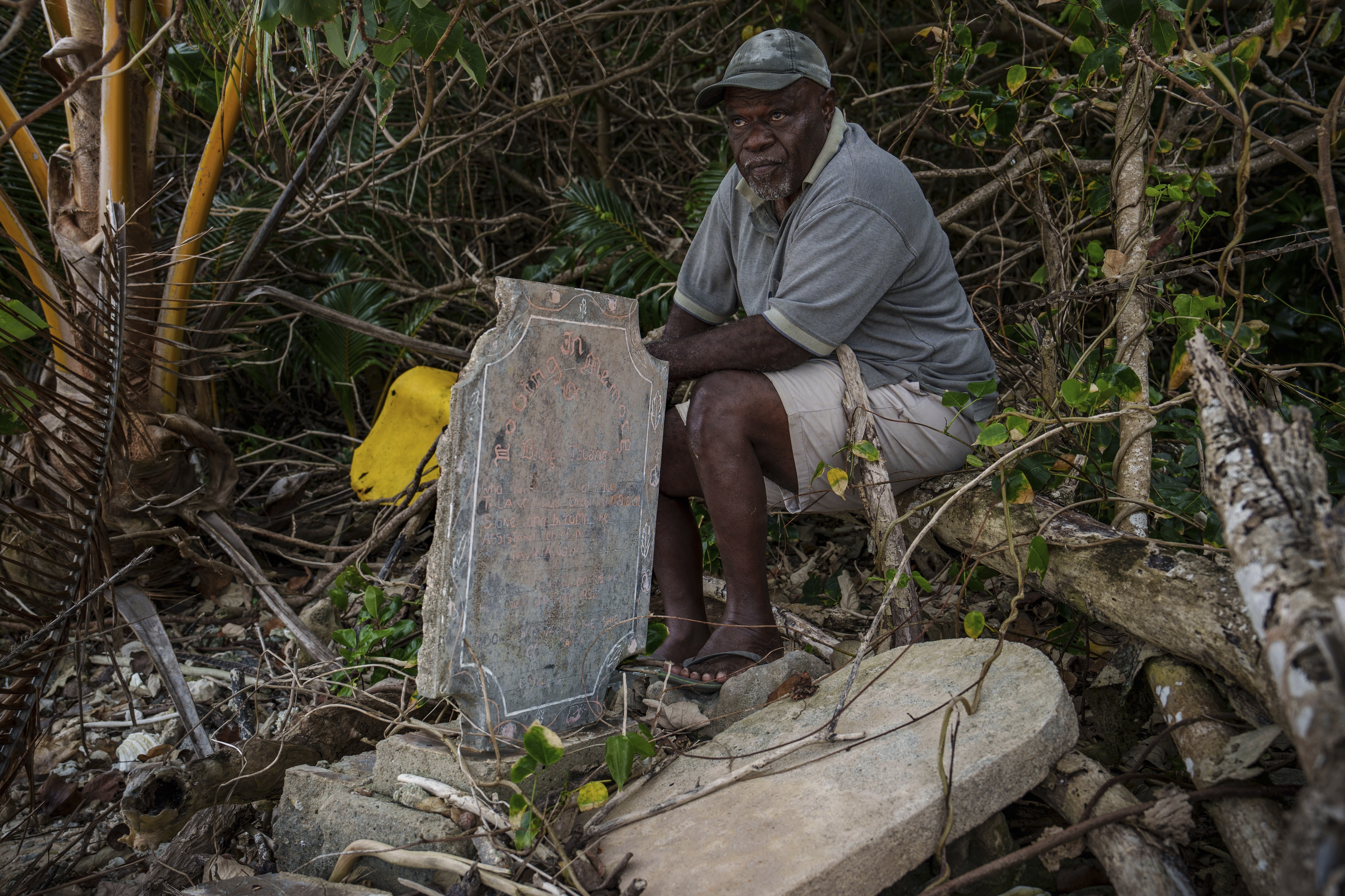 Village chief Amos Kalsont sits at his brother's grave on Pele Island, Vanuatu, just feet from the shoreline, where another headstone has been washed up on top of the site Friday, July 18, 2025. (AP Photo/Annika Hammerschlag)