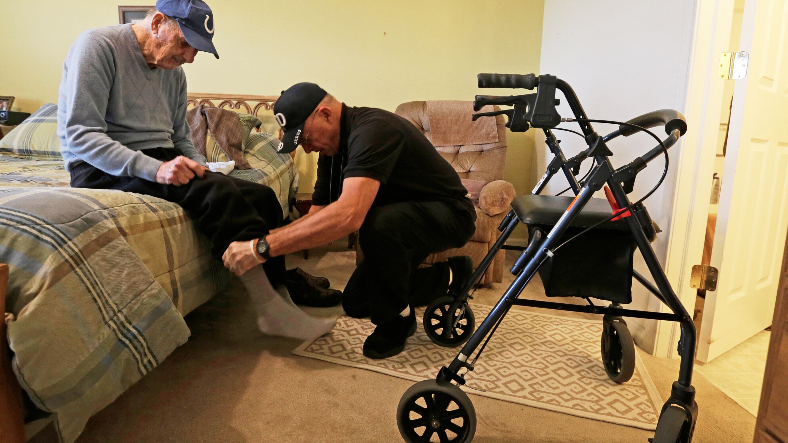 FILE - Caregiver Warren Manchess helping Paul Gregoline with his shoes and socks, in Noblesville, Ind., Nov. 27, 2013. (AP Photo/Darron Cummings, File)