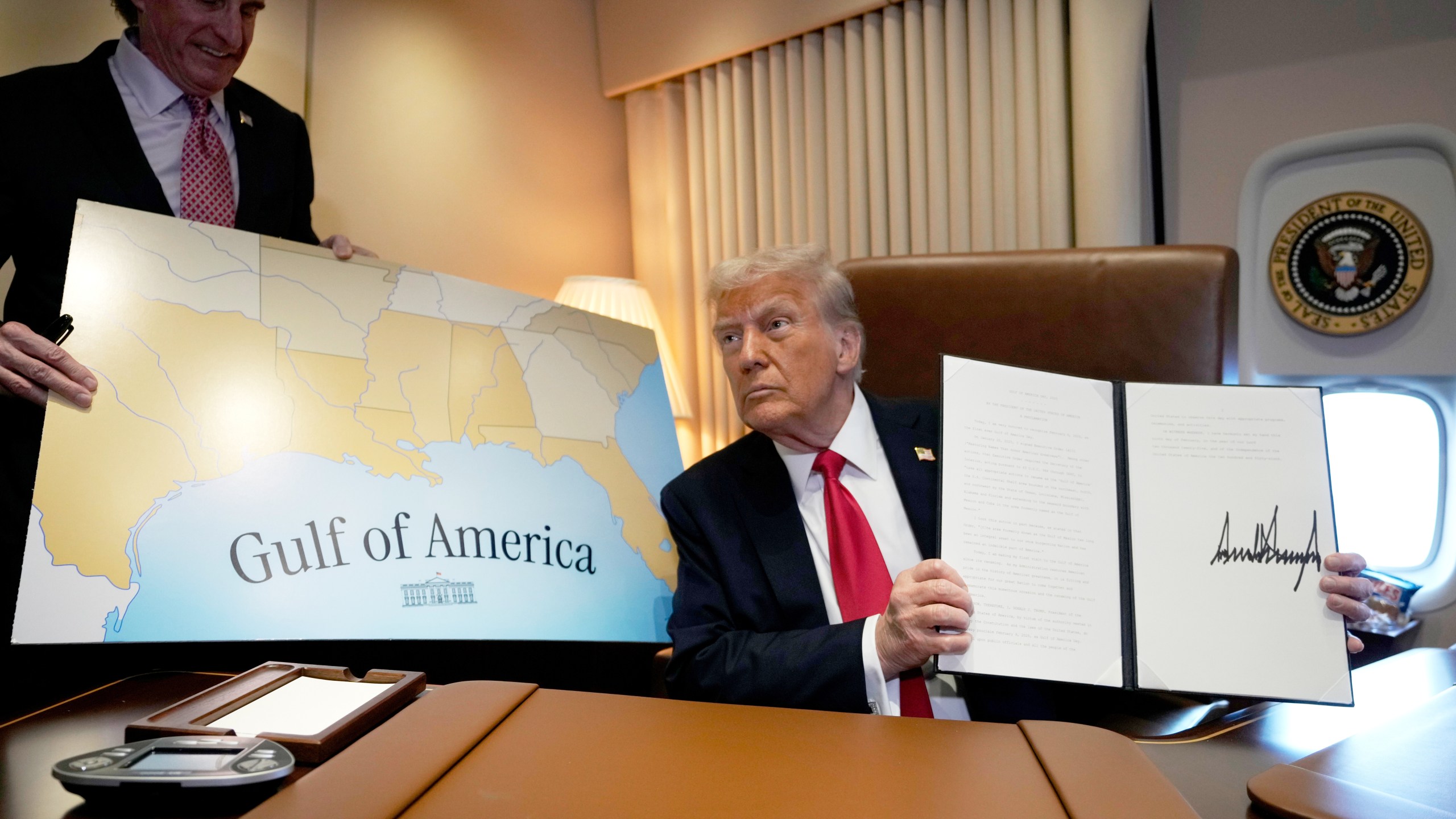 FILE - President Donald Trump holds up a signed proclamation declaring Feb. 9 Gulf of America Day, as Interior Secretary Doug Burgum watches aboard Air Force One as Trump travels from West Palm Beach, Fla. to New Orleans, Feb. 9, 2025. (AP Photo/Ben Curtis, File)