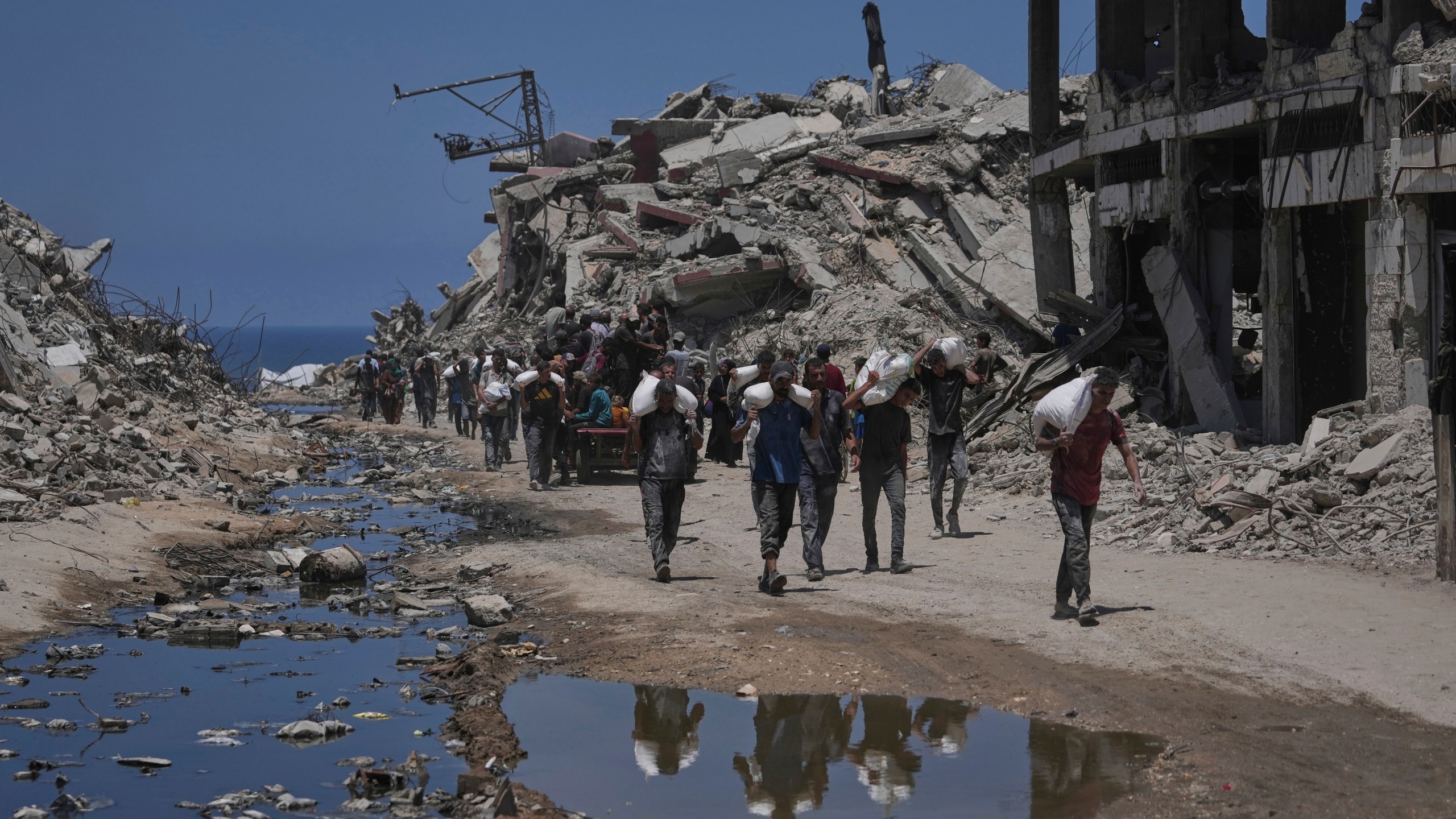 Palestinians carry sacks of flour unloaded from a humanitarian aid convoy that reached Gaza City from the northern Gaza Strip, Tuesday, July 22, 2025. (AP Photo/Jehad Alshrafi)
