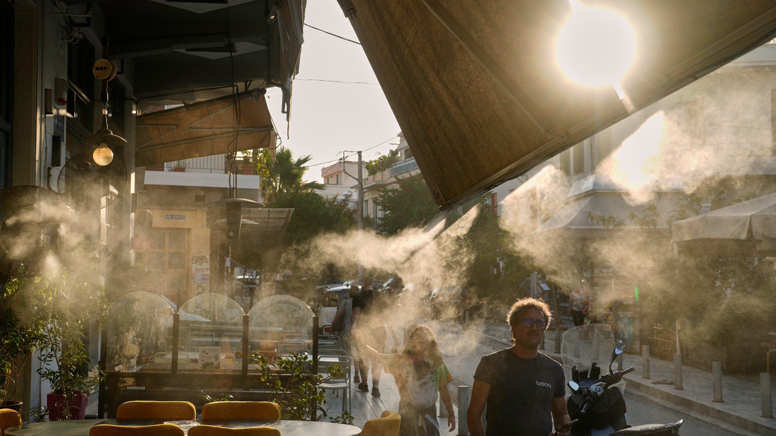 Pedestrians walk next to a mist machine in Thisio district of Athens during a heatwave, Tuesday, July 22, 2025.(AP Photo/Petros Giannakouris)
