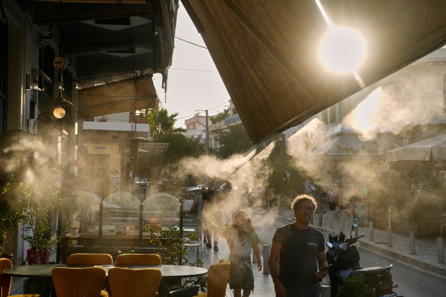 Pedestrians walk next to a mist machine in Thisio district of Athens during a heatwave, Tuesday, July 22, 2025.(AP Photo/Petros Giannakouris)