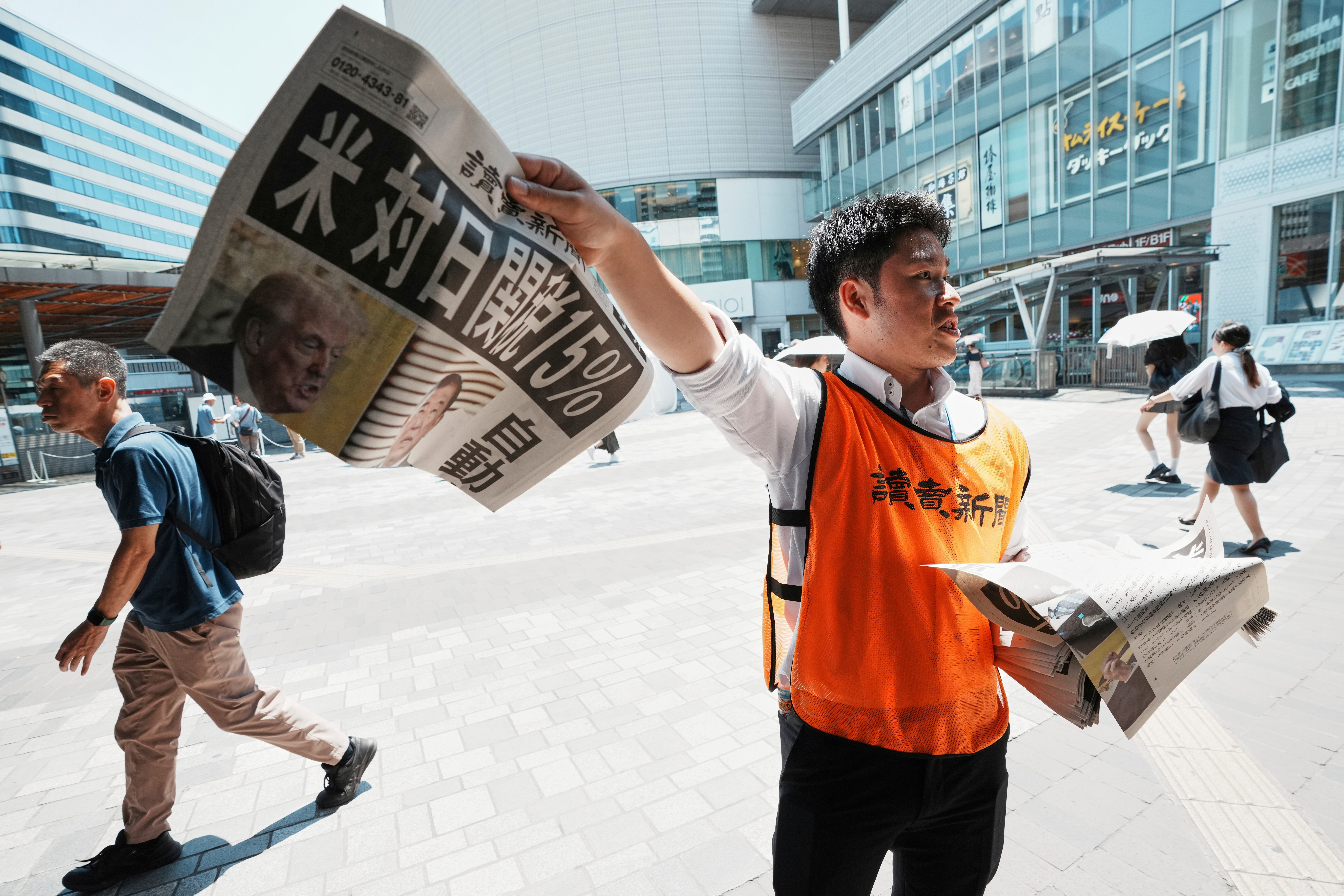 A staff member distributes an extra edition of the Yomiuri Shimbun newspaper reporting that President Donald Trump announced a trade framework with Japan on Tuesday, Wednesday, July 23, 2025, in Tokyo. The headline reads "U.S., a 15% tax on goods imported from Japan." (AP Photo/Eugene Hoshiko)