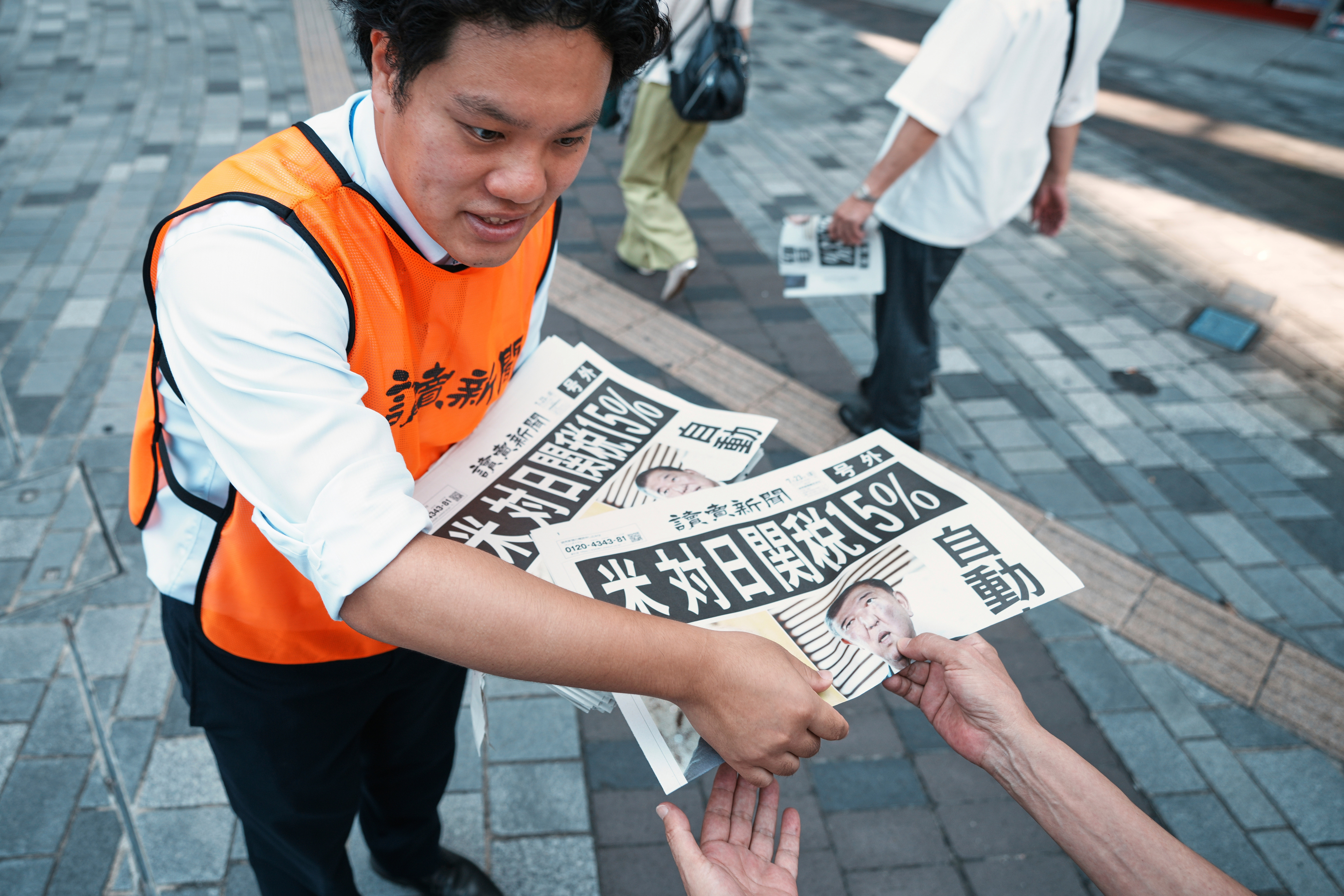A staff member distributes an extra edition of the Yomiuri Shimbun newspaper reporting that President Donald Trump announced a trade framework with Japan on Tuesday, Wednesday, July 23, 2025, in Tokyo. (AP Photo/Eugene Hoshiko)