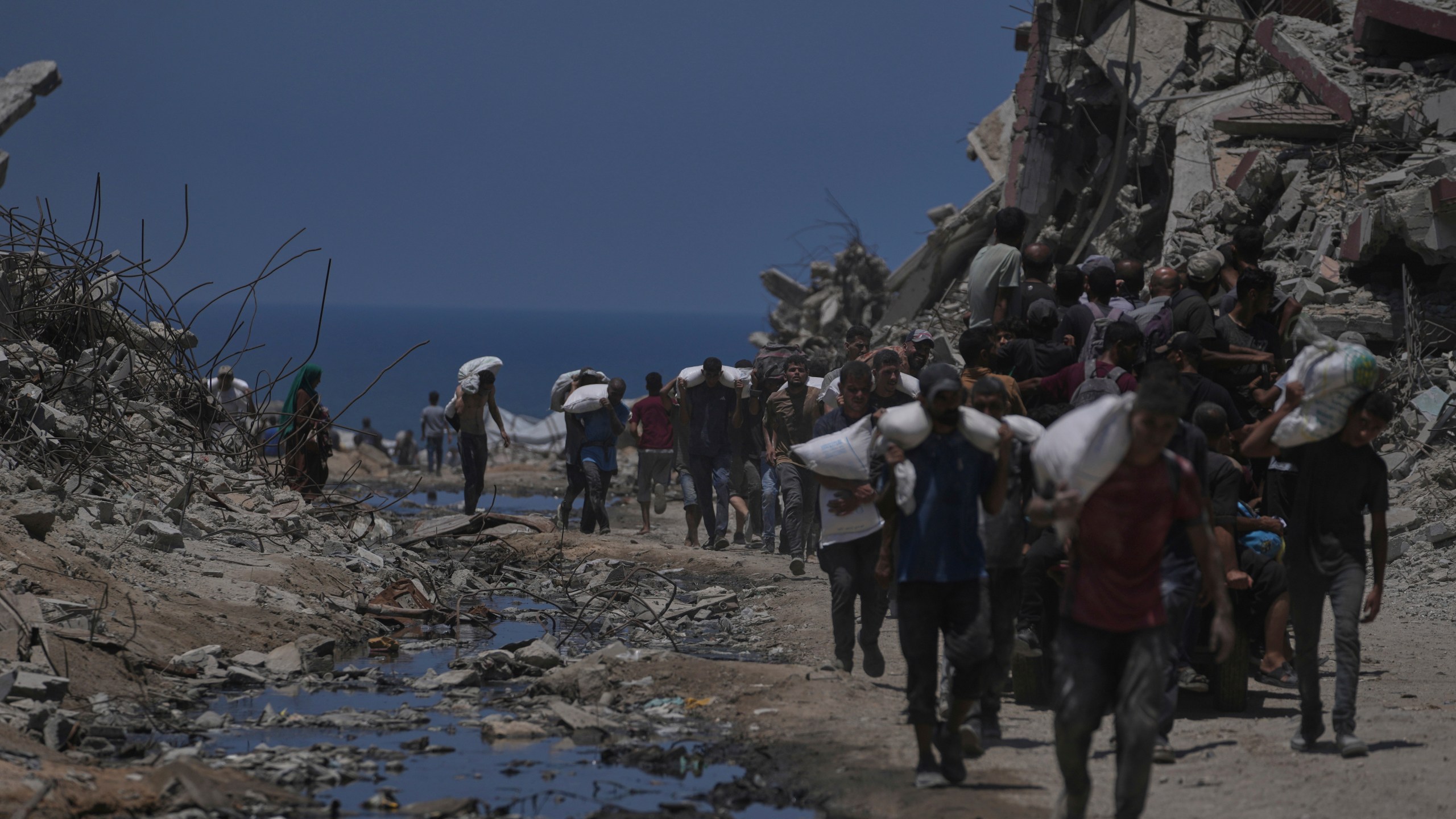 Palestinians carry sacks of flour unloaded from a humanitarian aid convoy that reached Gaza City from the northern Gaza Strip, Tuesday, July 22, 2025. (AP Photo/Jehad Alshrafi)