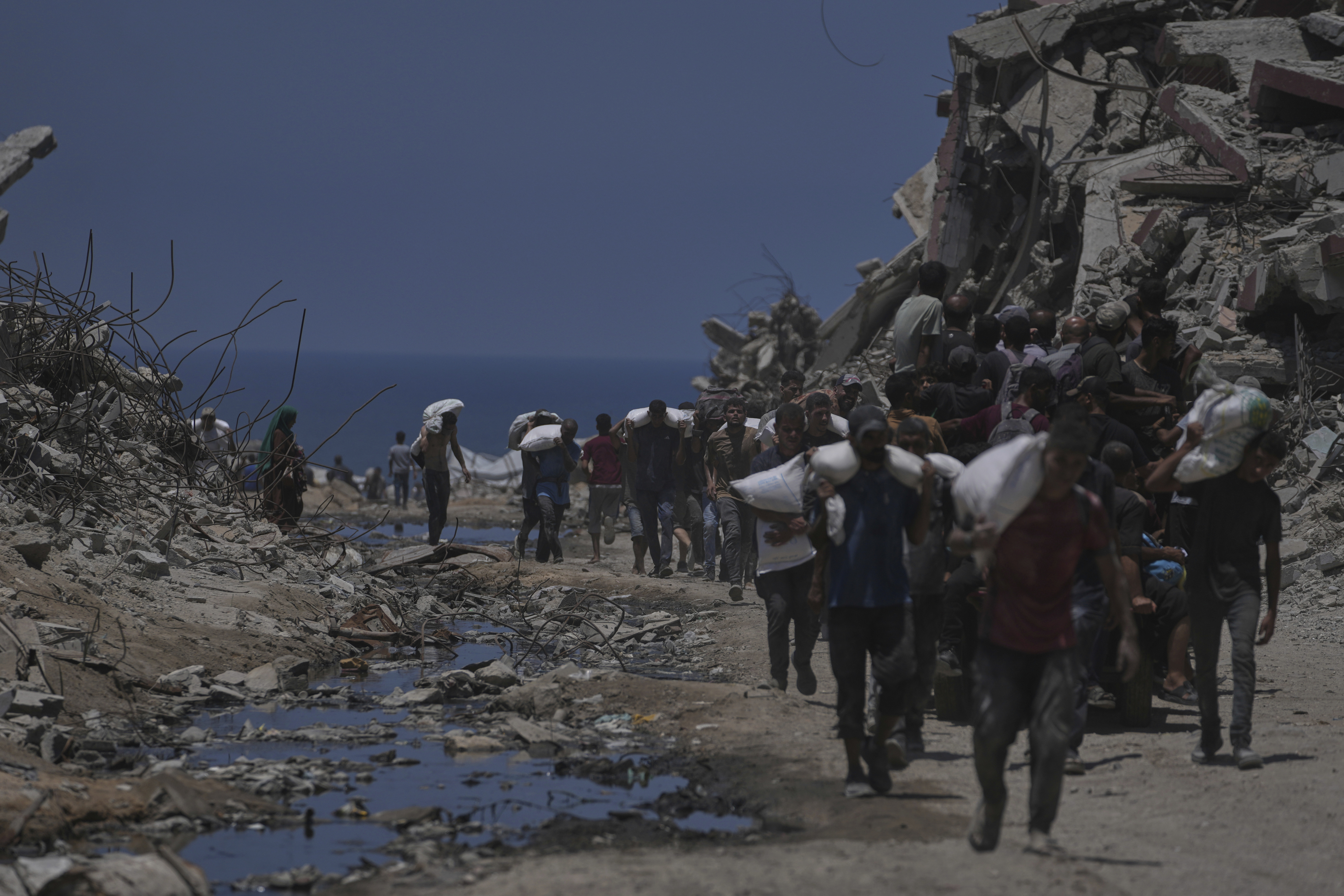 Palestinians carry sacks of flour unloaded from a humanitarian aid convoy that reached Gaza City from the northern Gaza Strip, Tuesday, July 22, 2025. (AP Photo/Jehad Alshrafi)