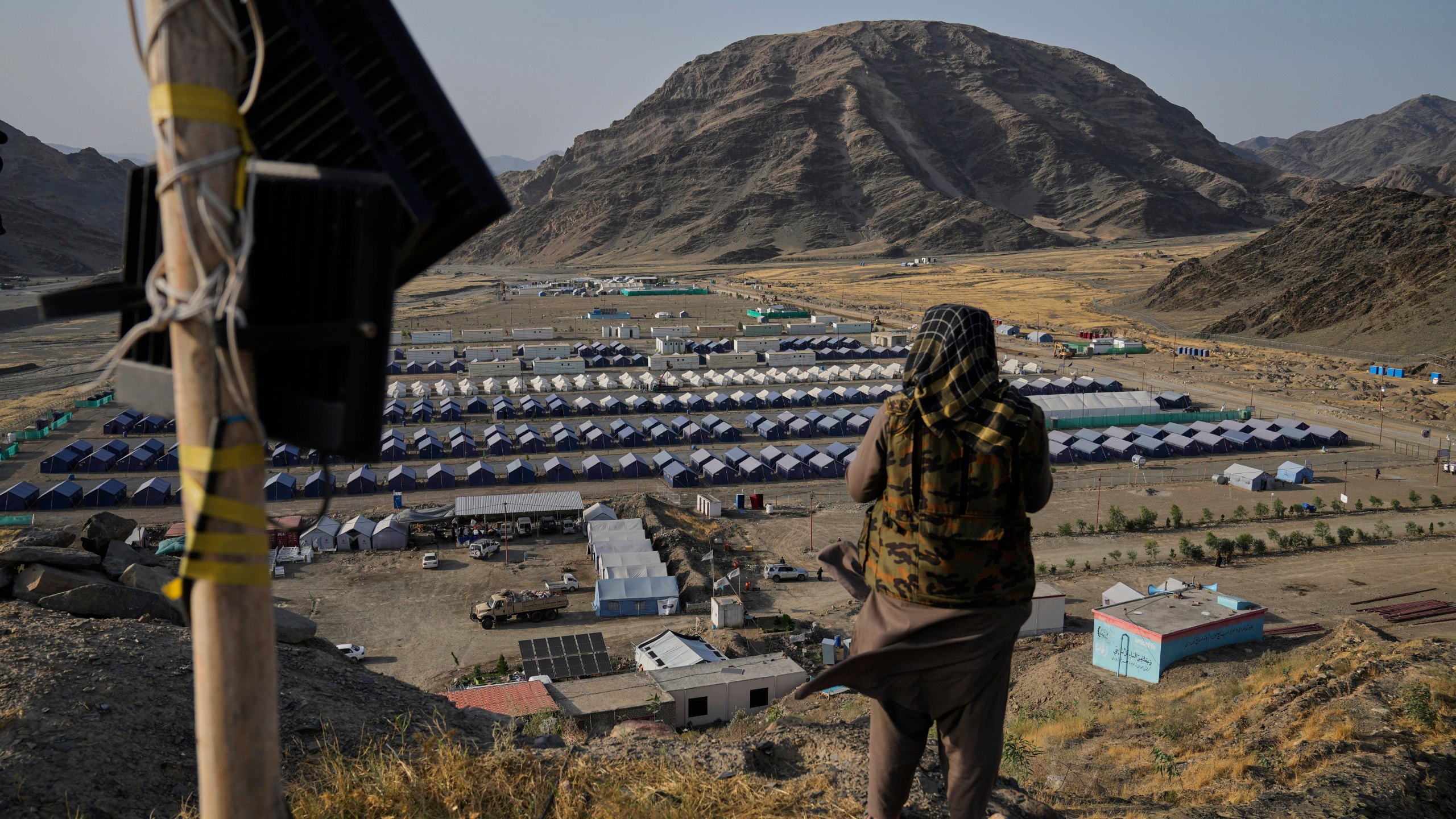 FILE -A Taliban fighter stands on a hill overlooking a camp housing Afghan refugees who have been repatriated from Pakistan, near the Pakistan-Afghanistan border, in Torkham, Afghanistan, May 31, 2025. (AP Photo/Ebrahim Noroozi, File)