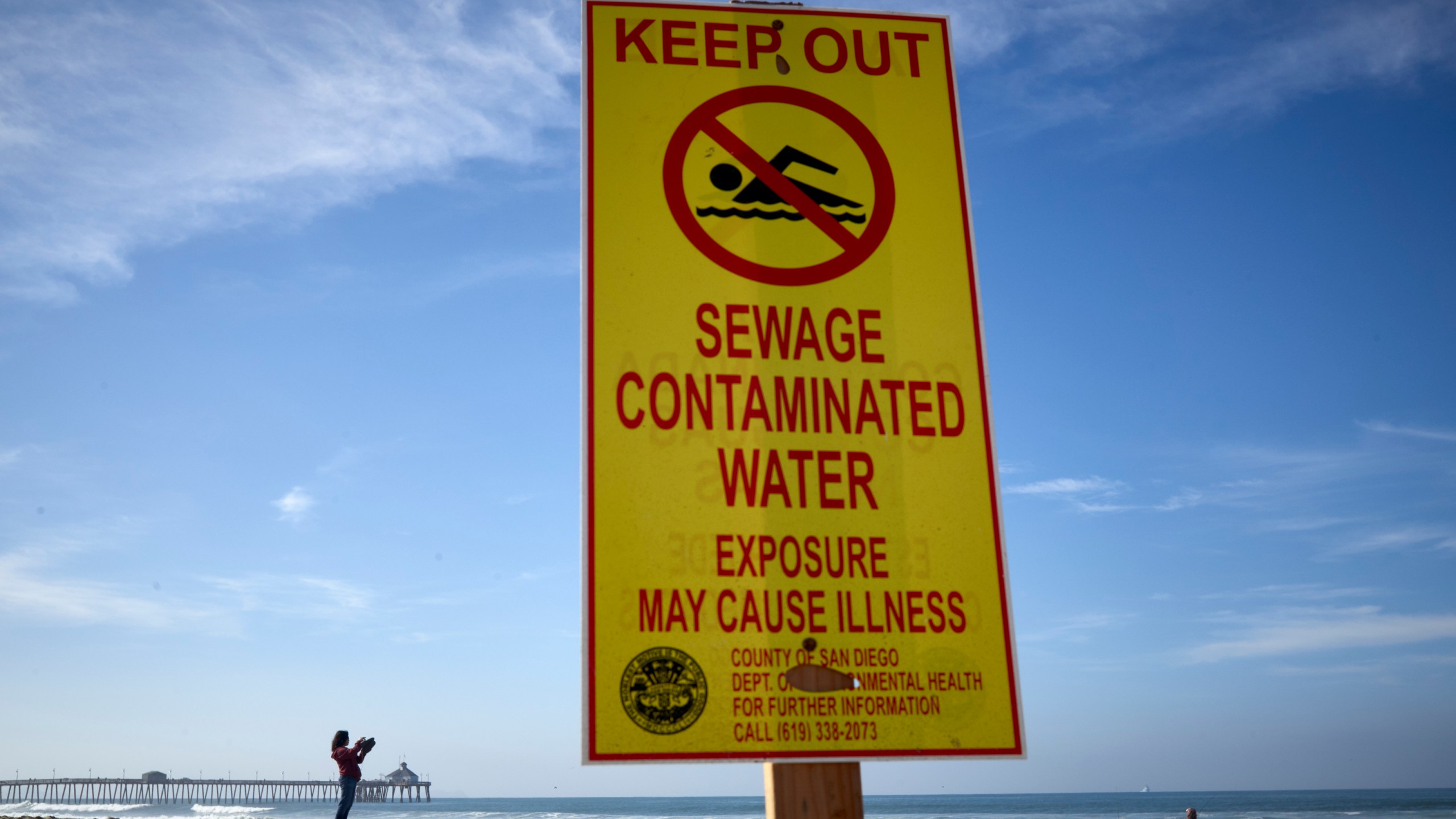 FILE - A woman records with a phone along the beach as a sign warns of contaminated water Dec. 12, 2018, at Imperial Beach, Calif. (AP Photo/Gregory Bull, File)