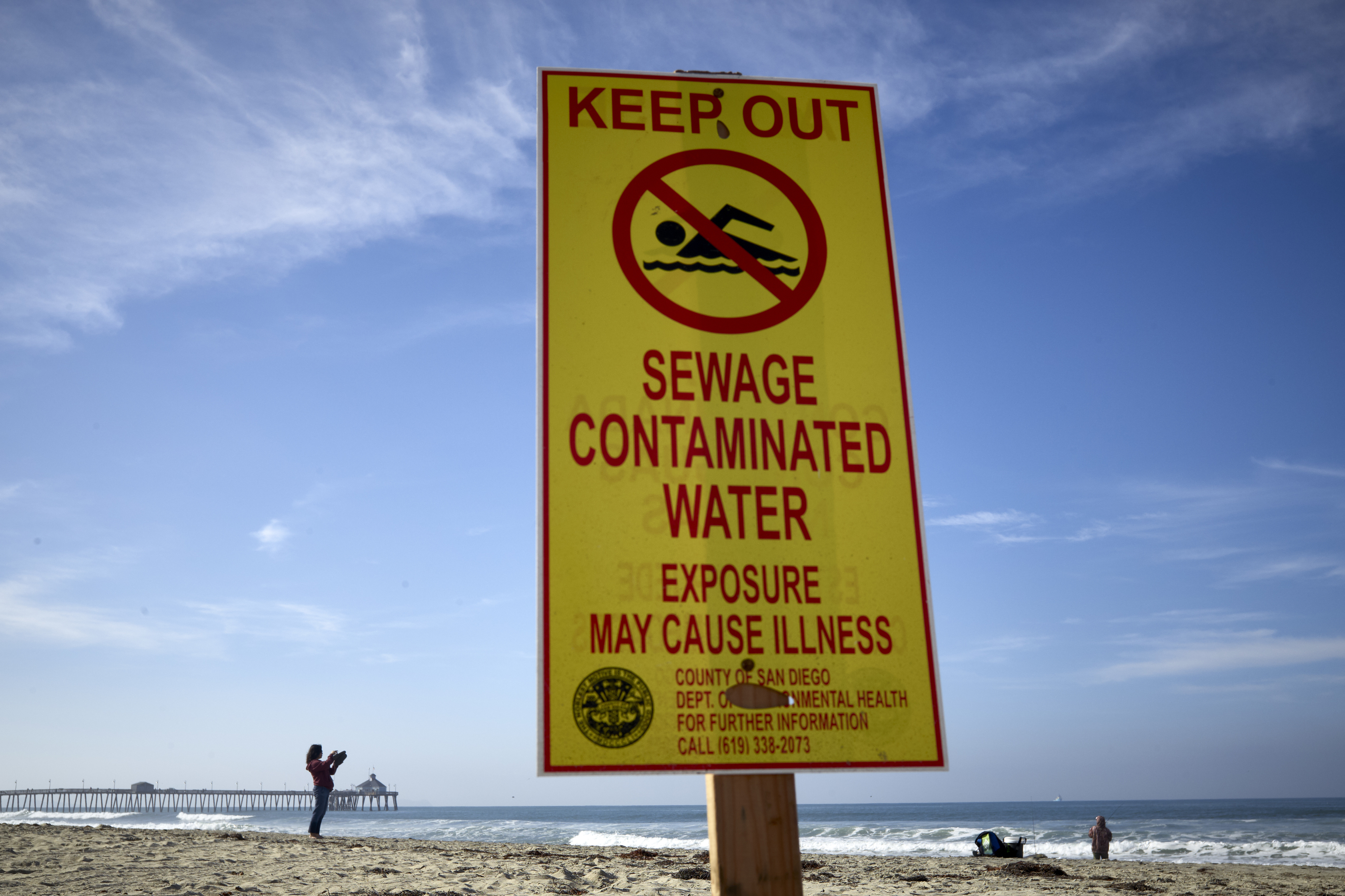 FILE - A woman records with a phone along the beach as a sign warns of contaminated water Dec. 12, 2018, at Imperial Beach, Calif. (AP Photo/Gregory Bull, File)