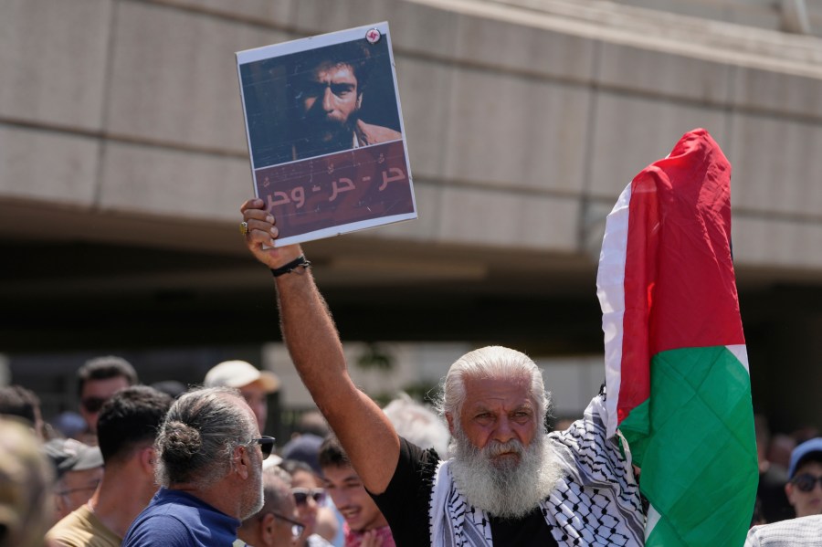 A supporter of Lebanese pro-Palestinian militant George Abdallah, who was serving a life sentence for complicity in the 1982 murders of an American and an Israeli diplomat in Paris, holds up a poster with his portrait and a Palestinian flag as he waits for Abdallah's arrival at Rafik Hariri International Airport in Beirut, Lebanon, Friday, July 25, 2025. The Arabic reads: "Free, free, and free" (AP Photo/Hussein Malla)