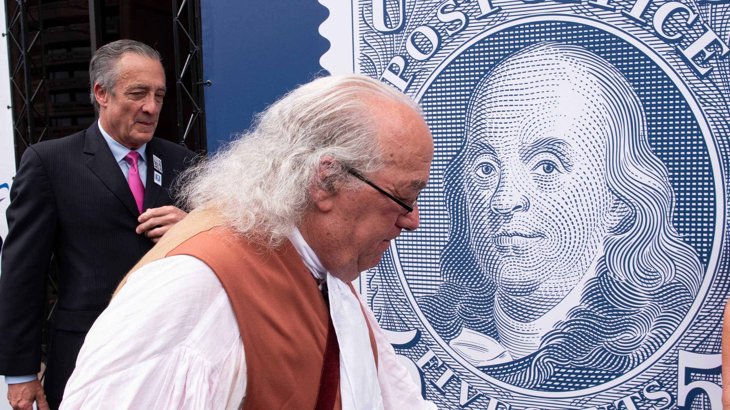 FILE - Barry Stevens, portraying Benjamin Franklin, right, walks past a just unveiled stamp marking the 250th anniversary of the postal service, Wednesday, July 23, 2025, in Washington, as Postmaster General David Steiner looks on. (AP Photo/Cliff Owen, File)