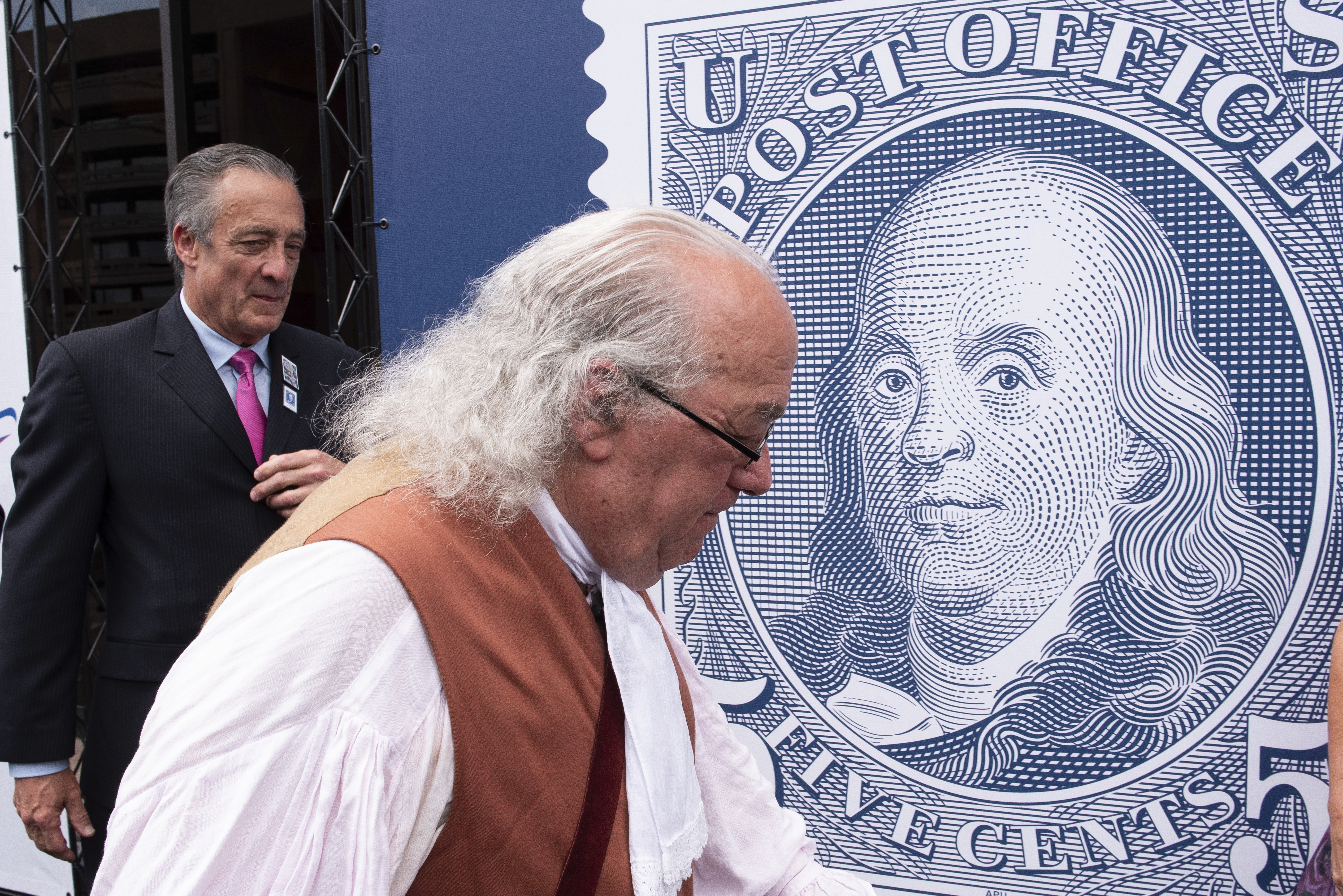 FILE - Barry Stevens, portraying Benjamin Franklin, right, walks past a just unveiled stamp marking the 250th anniversary of the postal service, Wednesday, July 23, 2025, in Washington, as Postmaster General David Steiner looks on. (AP Photo/Cliff Owen, File)