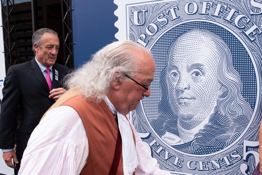 FILE - Barry Stevens, portraying Benjamin Franklin, right, walks past a just unveiled stamp marking the 250th anniversary of the postal service, Wednesday, July 23, 2025, in Washington, as Postmaster General David Steiner looks on. (AP Photo/Cliff Owen, File)
