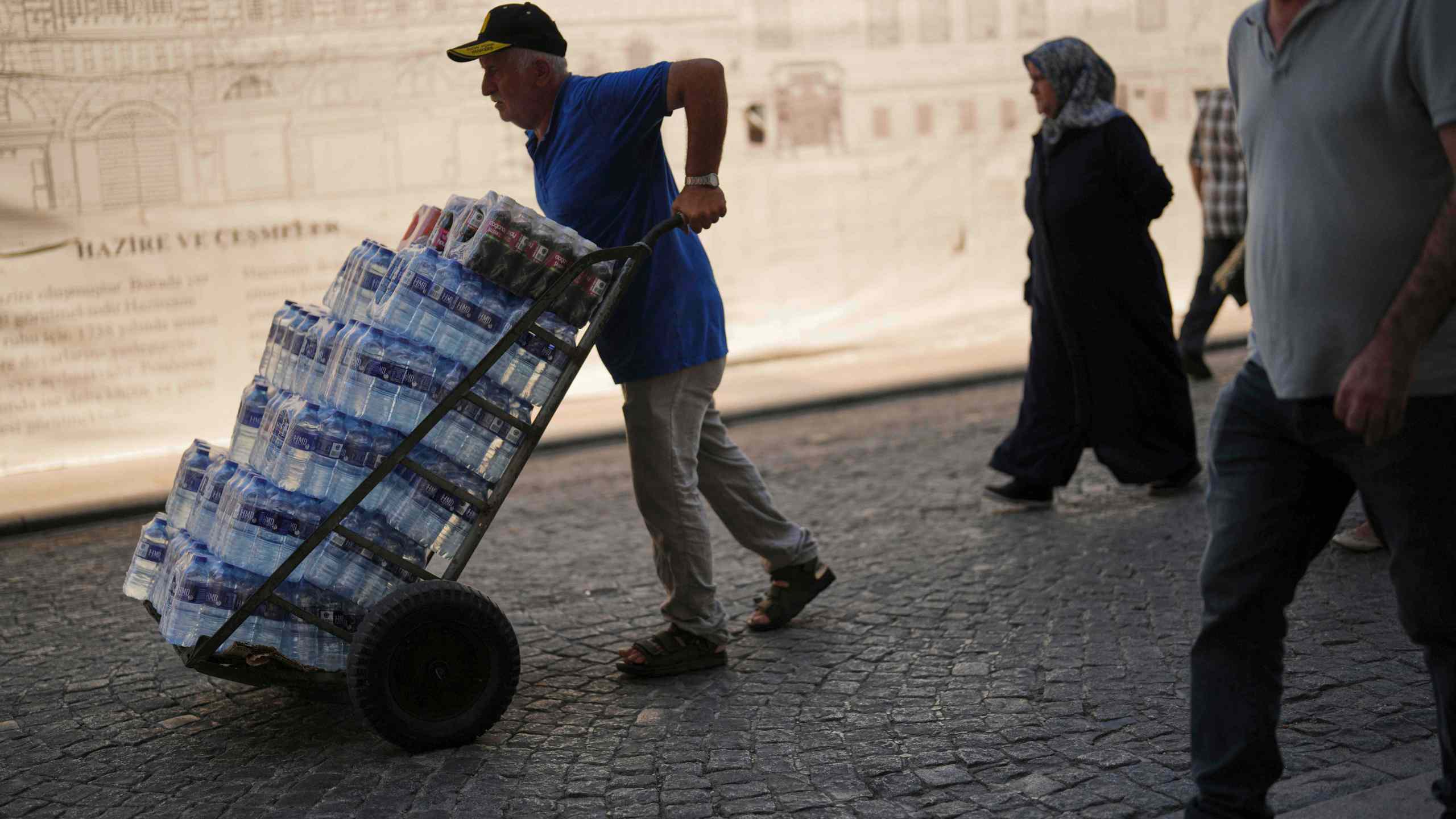 A man delivers plastic bottles of water to a local restaurant on a hot summer day at Eminonu district, in Istanbul, Turkey, Friday, July 25, 2025. (AP Photo/Francisco Seco)
