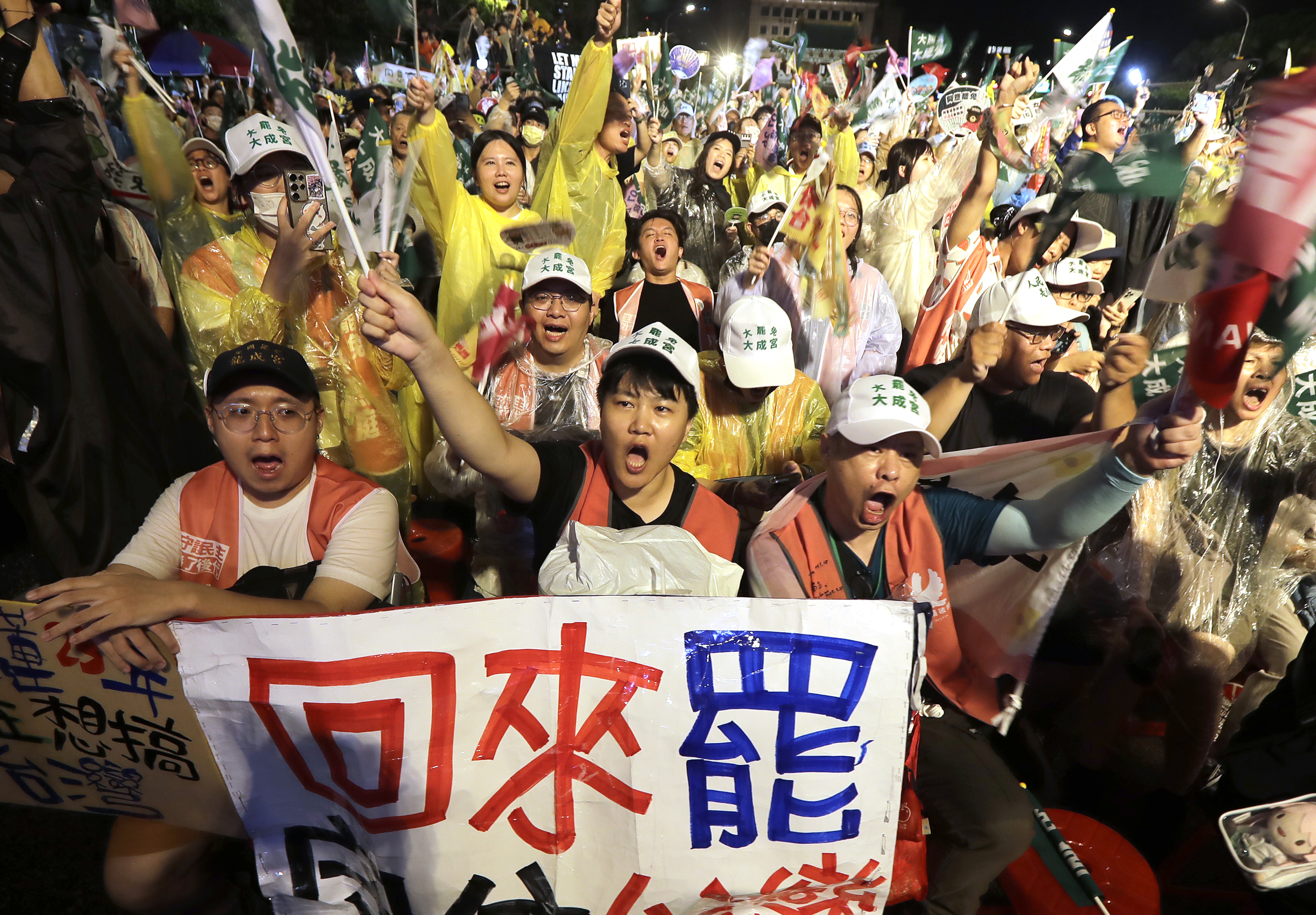 People shoot and hold a slogan reading ''Come Back to Recall'' during a campaign rally to promote recall vote targeting 24 Nationalist Party (KMT) lawmakers in Taipei, Taiwan, Thursday, July 24, 2025. (AP Photo/Chiang Ying-ying)