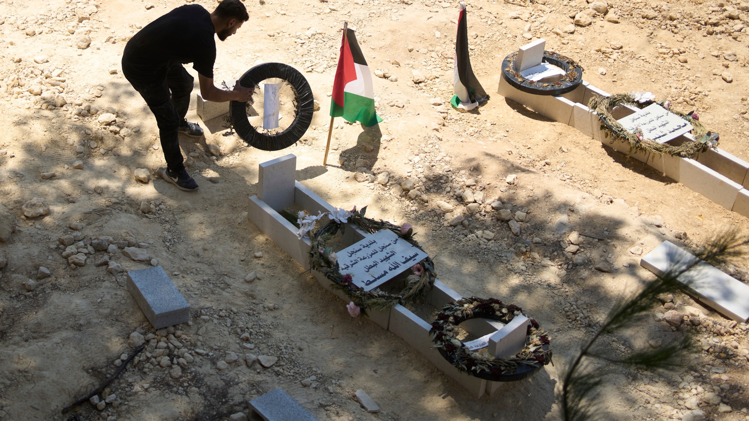 On Monday, July 21, 2025, a man tidies the graves of Palestinian-American Sayfollah Musallet, left, and Mohammed al-Shalabi, both of whom were killed by Israeli settlers in the West Bank town of Al Mazra as-Sharqiya. (AP Photo/Maya Alleruzzo)