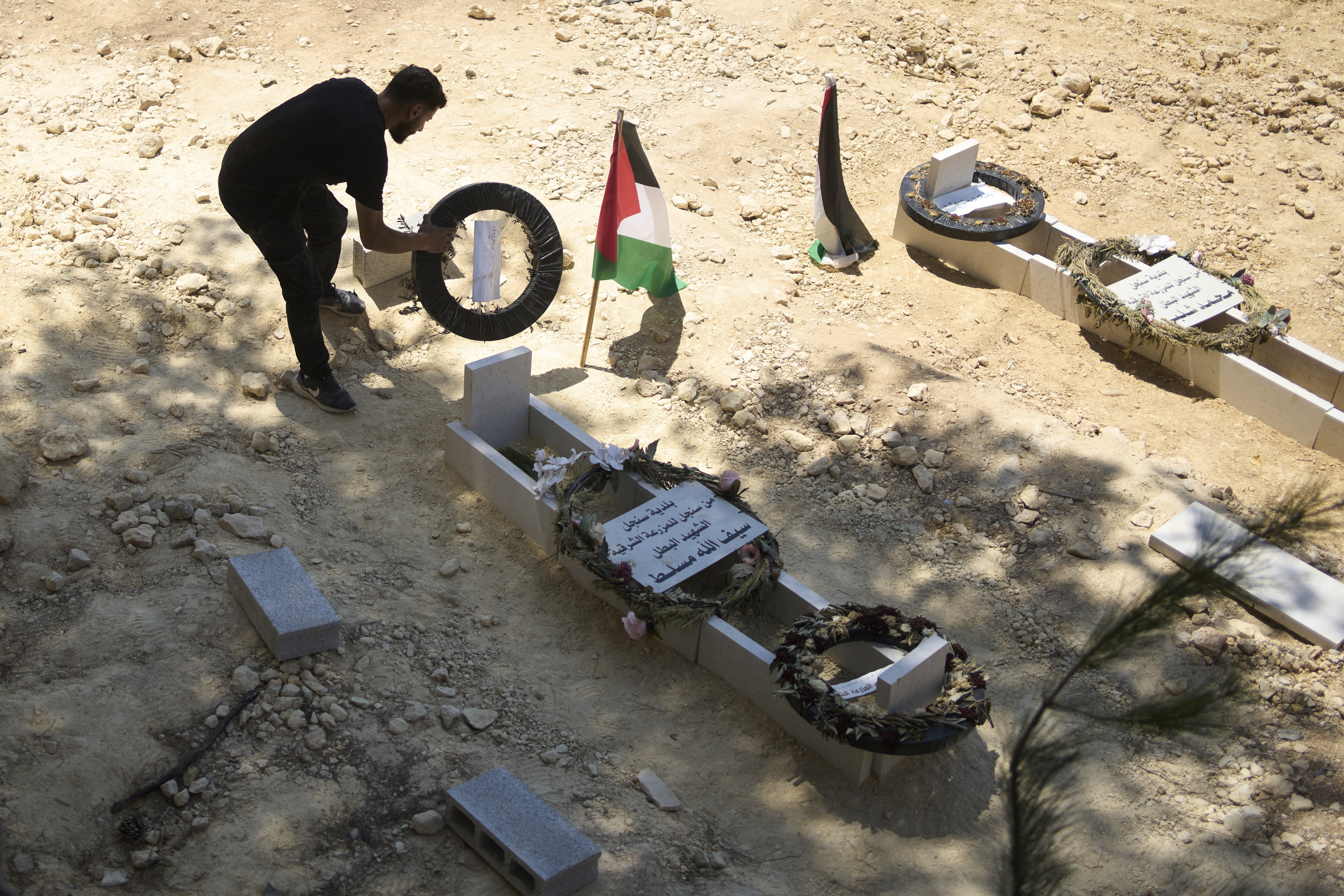 On Monday, July 21, 2025, a man tidies the graves of Palestinian-American Sayfollah Musallet, left, and Mohammed al-Shalabi, both of whom were killed by Israeli settlers in the West Bank town of Al Mazra as-Sharqiya. (AP Photo/Maya Alleruzzo)