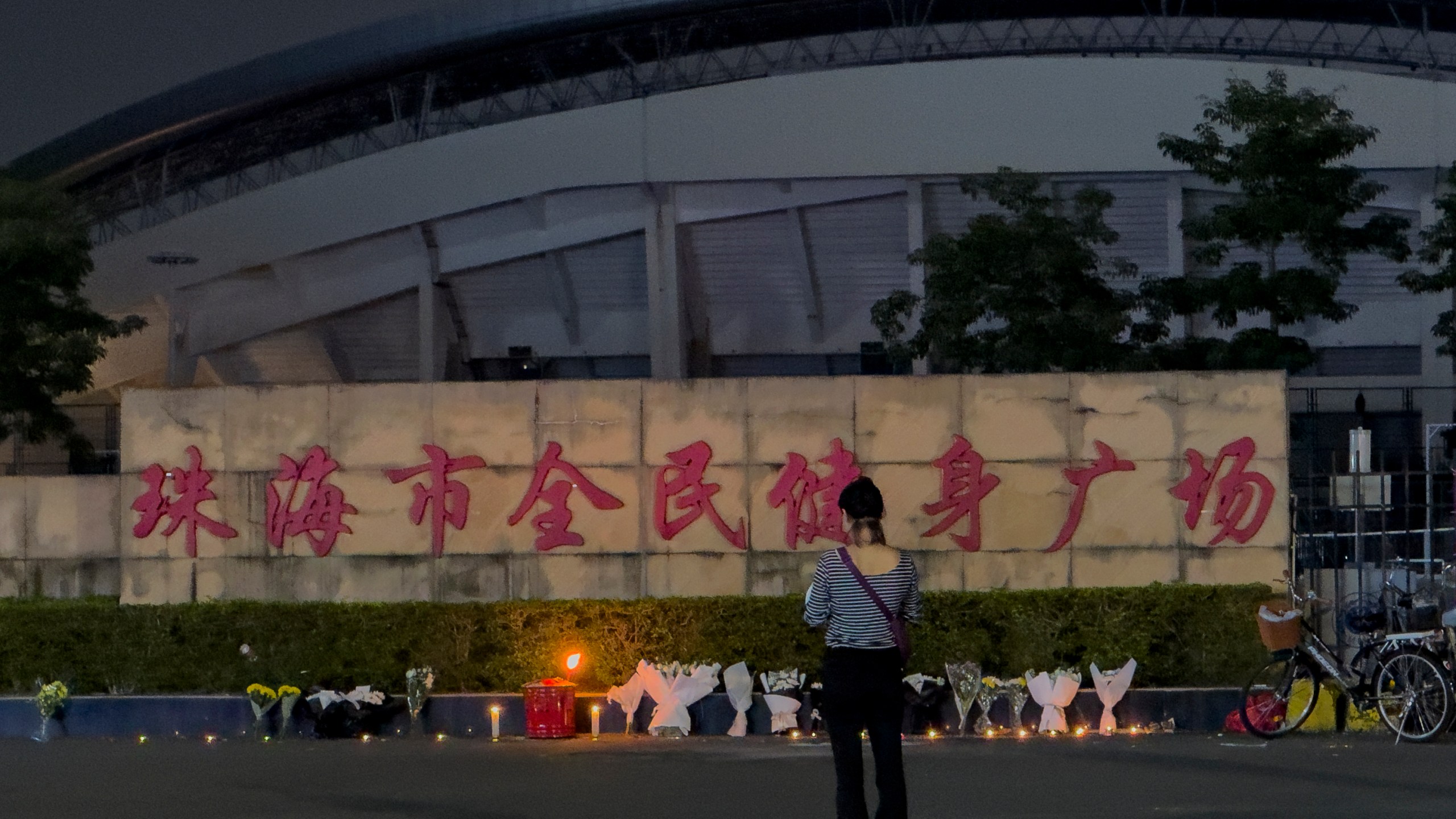 FILE - A woman stands near flowers placed outside the "Zhuhai People's Fitness Plaza", where a man deliberately rammed his car into people exercising at the sports center, killing some and injuring others in Zhuhai in southern China's Guangdong province on Nov. 12, 2024. (AP Photo/Ng Han Guan, File)