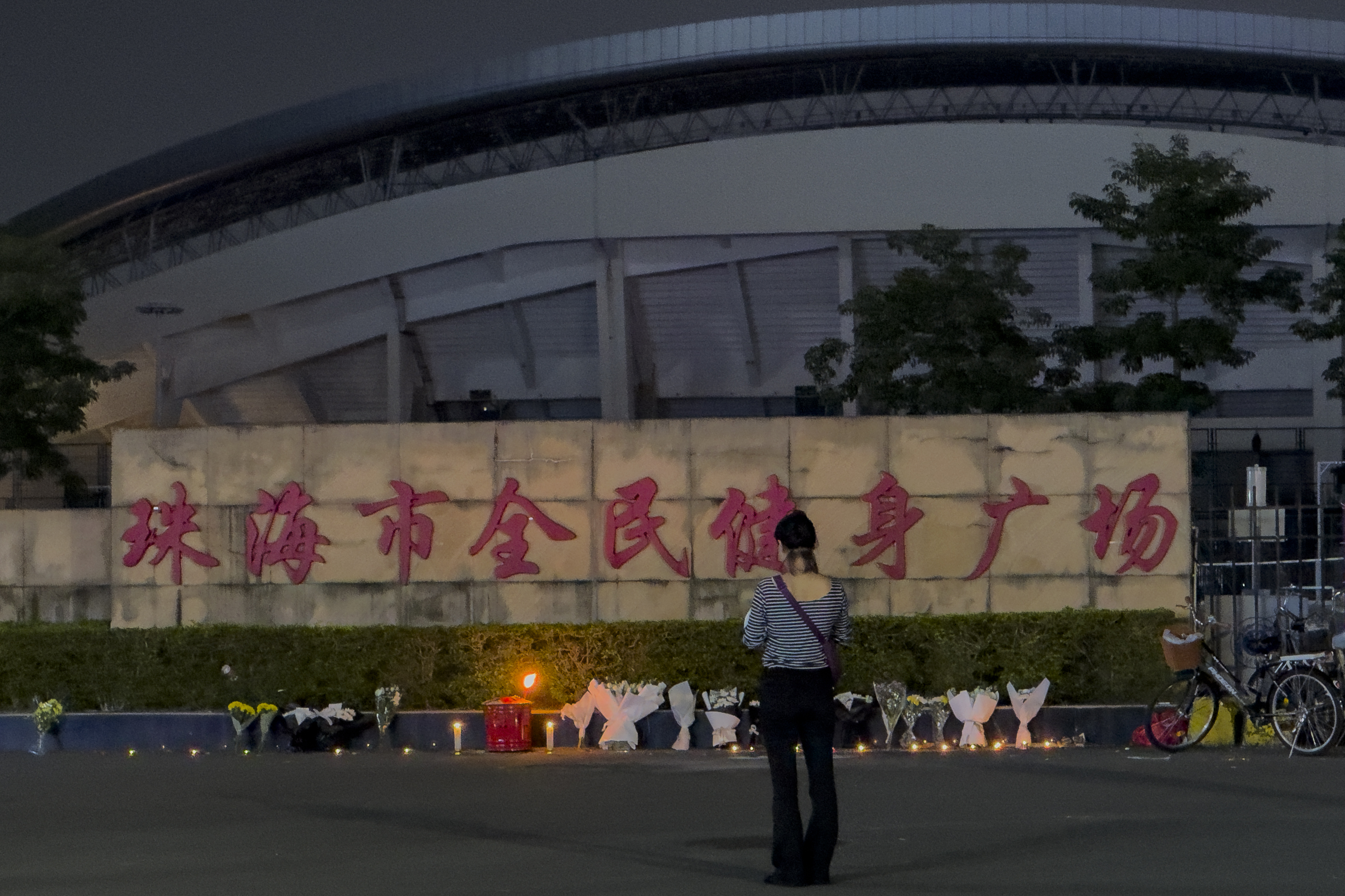 FILE - A woman stands near flowers placed outside the "Zhuhai People's Fitness Plaza", where a man deliberately rammed his car into people exercising at the sports center, killing some and injuring others in Zhuhai in southern China's Guangdong province on Nov. 12, 2024. (AP Photo/Ng Han Guan, File)