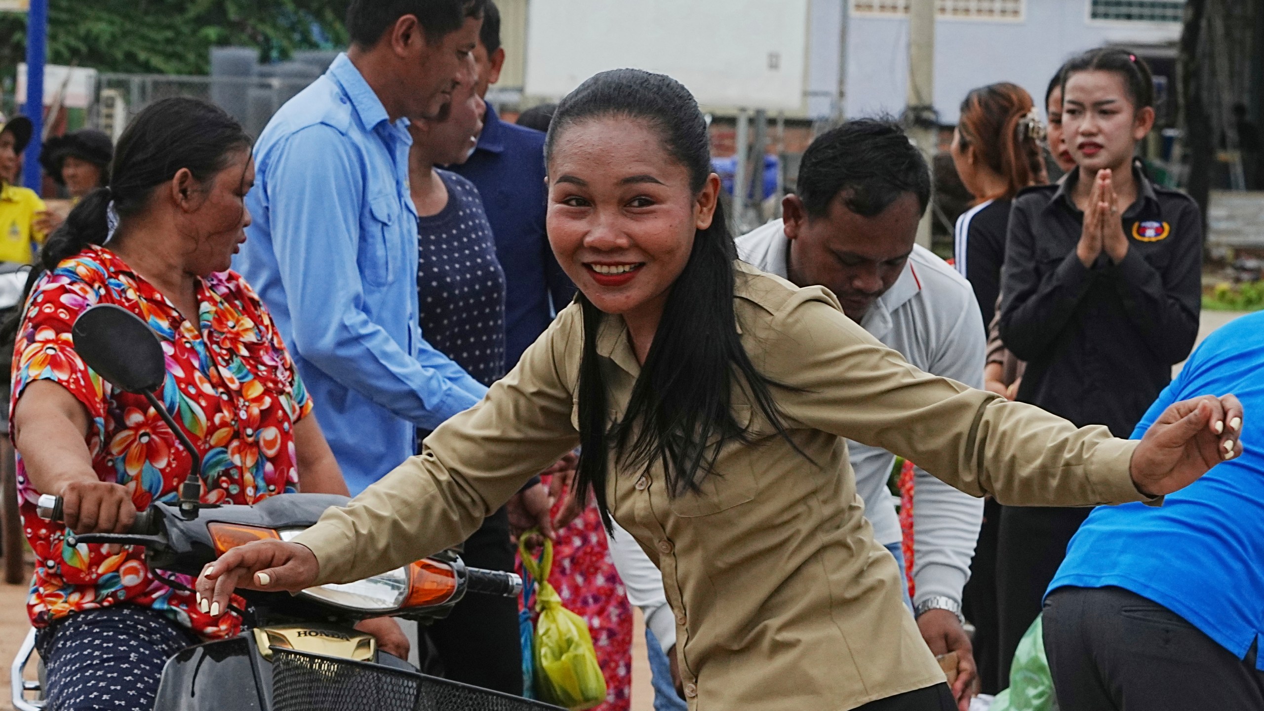A Cambodian youth volunteer Chhar Sin, foreground, greats villagers who donate their personal belongings for the displacing people at a sidewalk in Srey Snam district in Siem Reap province, Cambodia, Saturday, July 26, 2025, during fighting between Thailand and Cambodia. (AP Photo/Heng Sinith)