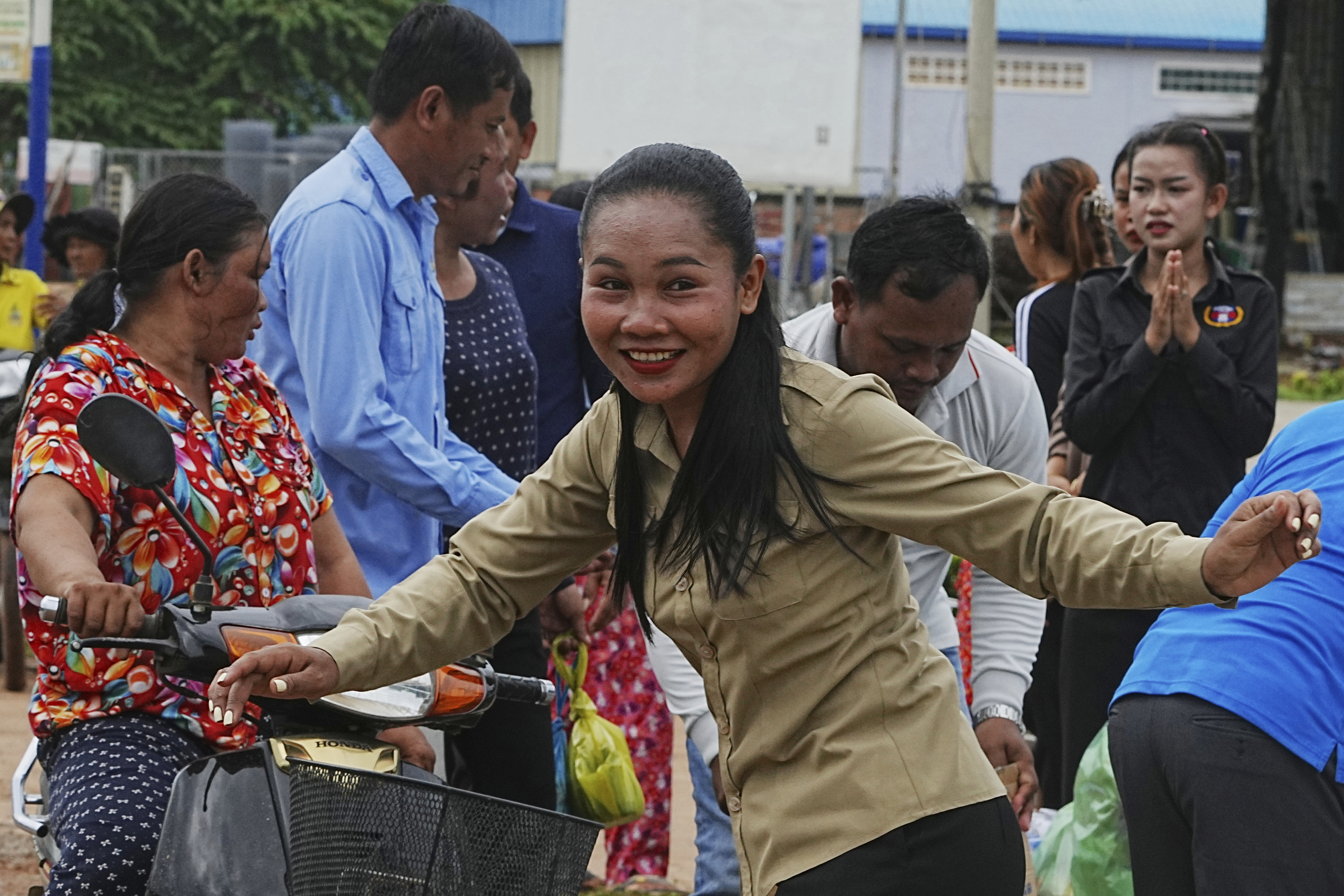 A Cambodian youth volunteer Chhar Sin, foreground, greats villagers who donate their personal belongings for the displacing people at a sidewalk in Srey Snam district in Siem Reap province, Cambodia, Saturday, July 26, 2025, during fighting between Thailand and Cambodia. (AP Photo/Heng Sinith)