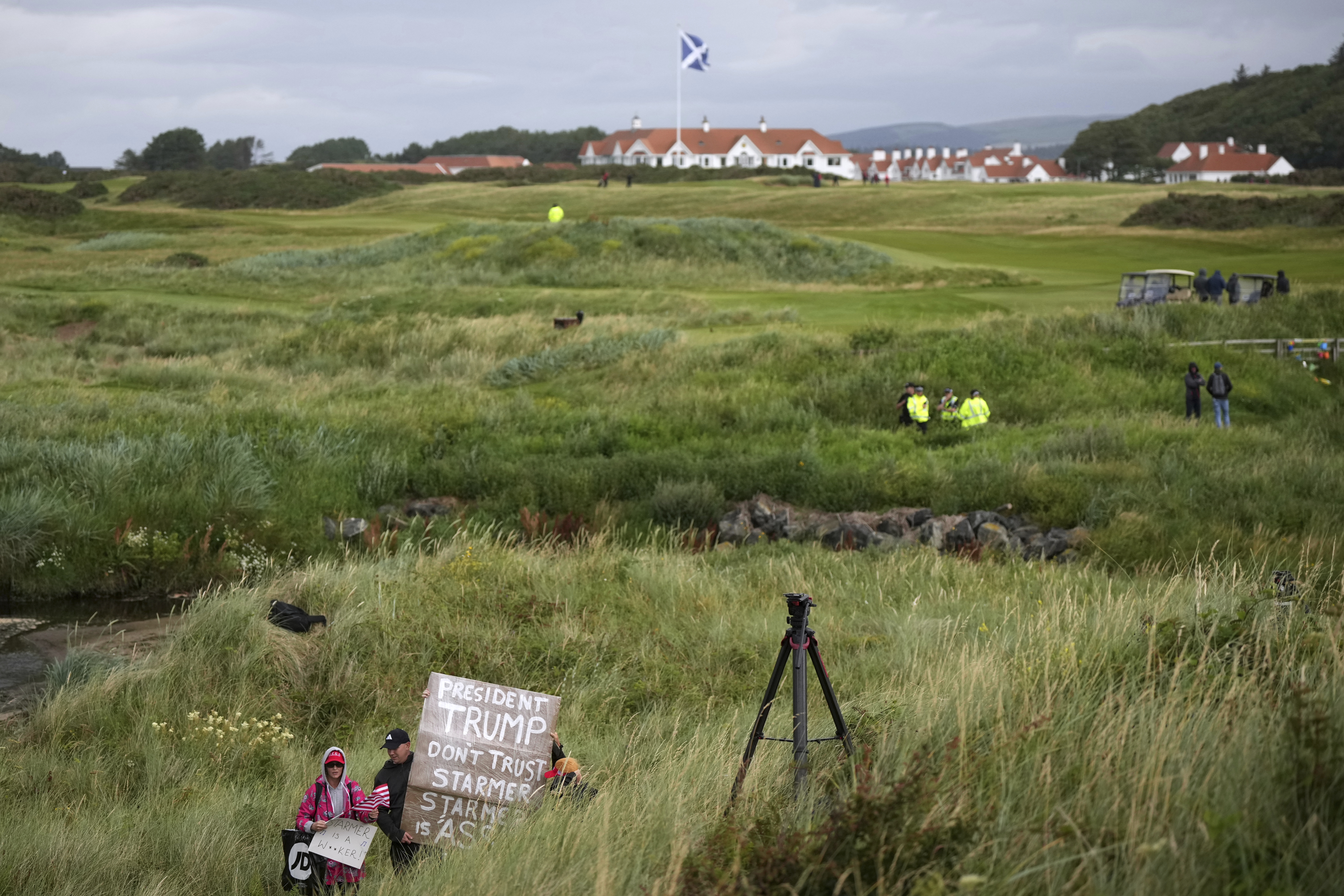 EDS NOTE: OBSCENITY - Trump supporters are watched by police and security forces as they hold signs near the Trump Turnberry golf course where President Donald Trump resides during his stay in Turnberry, Scotland, Sunday, July 27, 2025. (AP Photo/Alastair Grant)