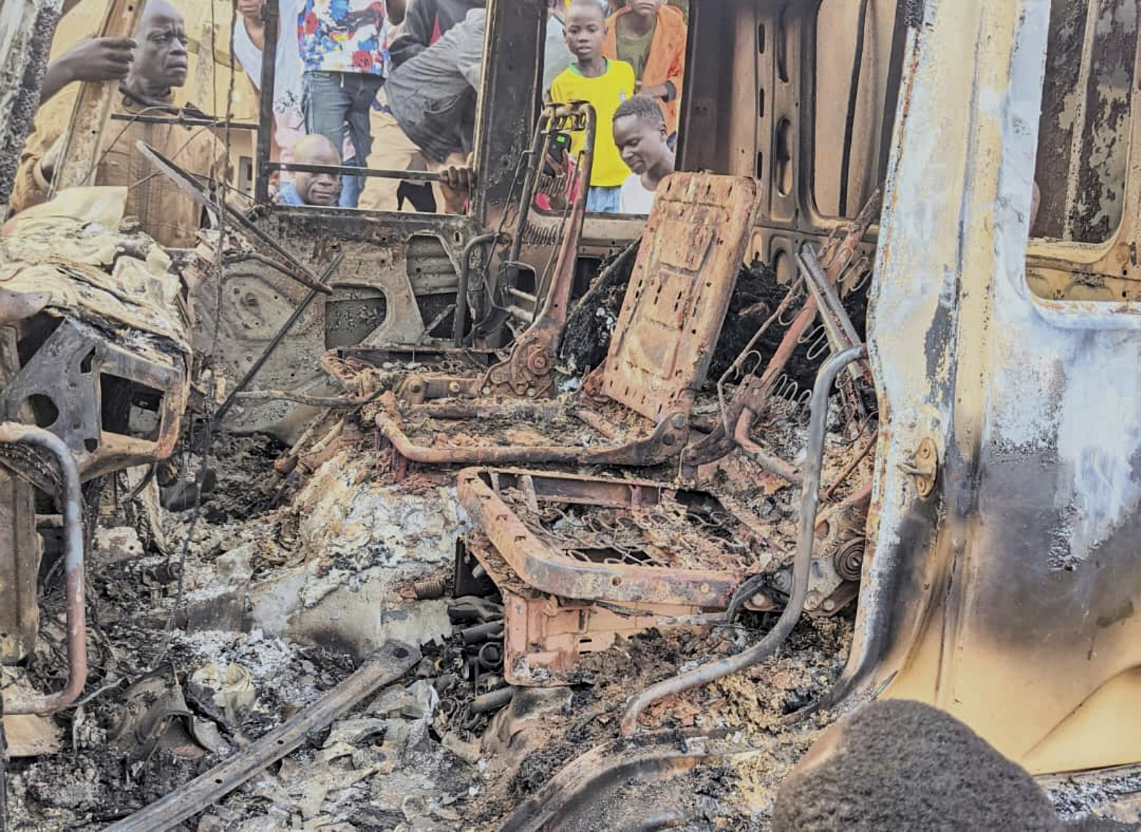 People gather around the charred remains of a burned vehicle following a deadly attack in Komanda, Ituri province of eastern Congo, Sunday, July 27, 2025. (Olivier Okande/UGC via AP)