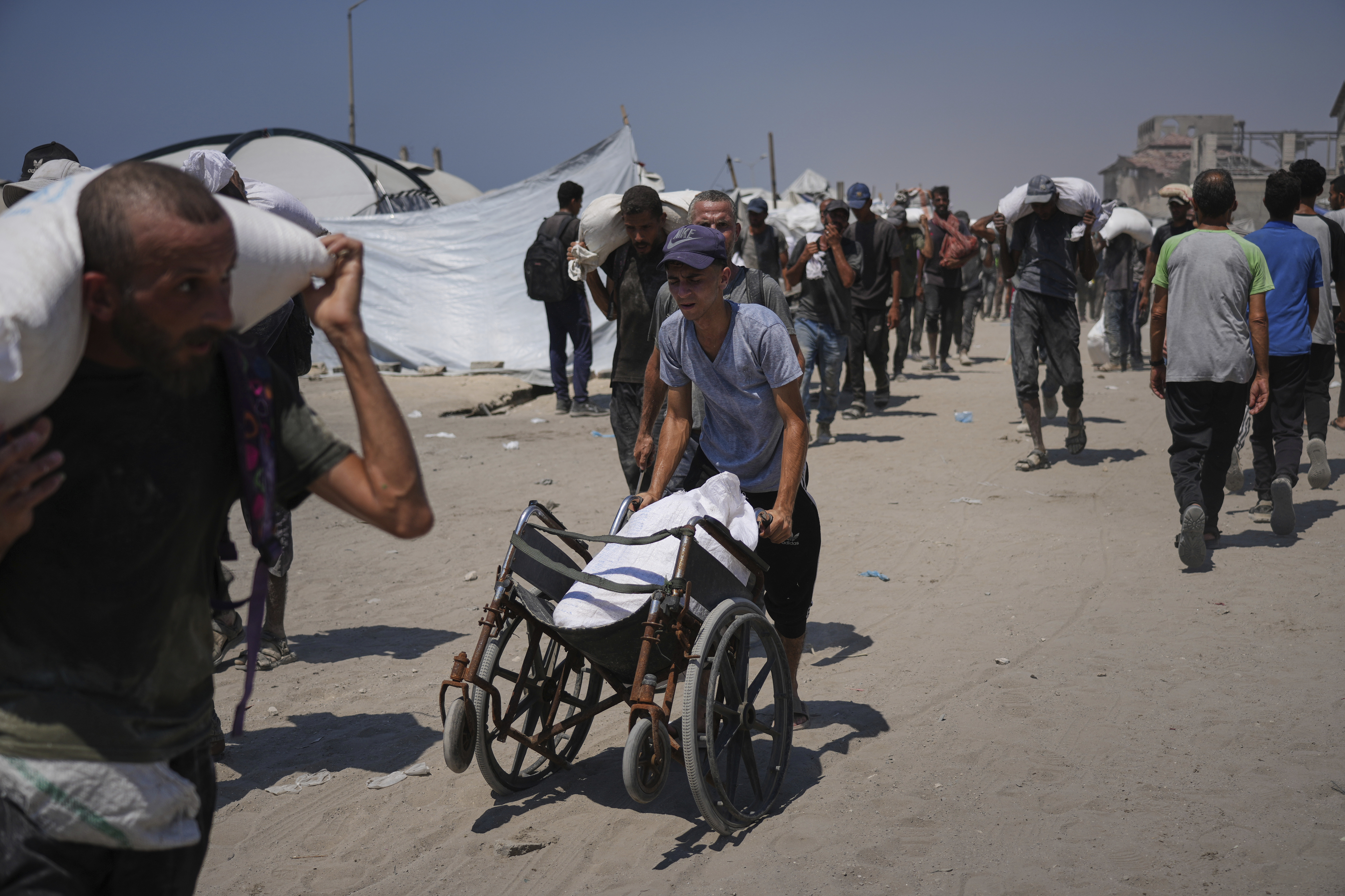 Palestinians carry sacks of flour unloaded from a humanitarian aid convoy that reached Gaza City from the northern Gaza Strip, Sunday, July 27, 2025. (AP Photo/Abdel Kareem Hana)