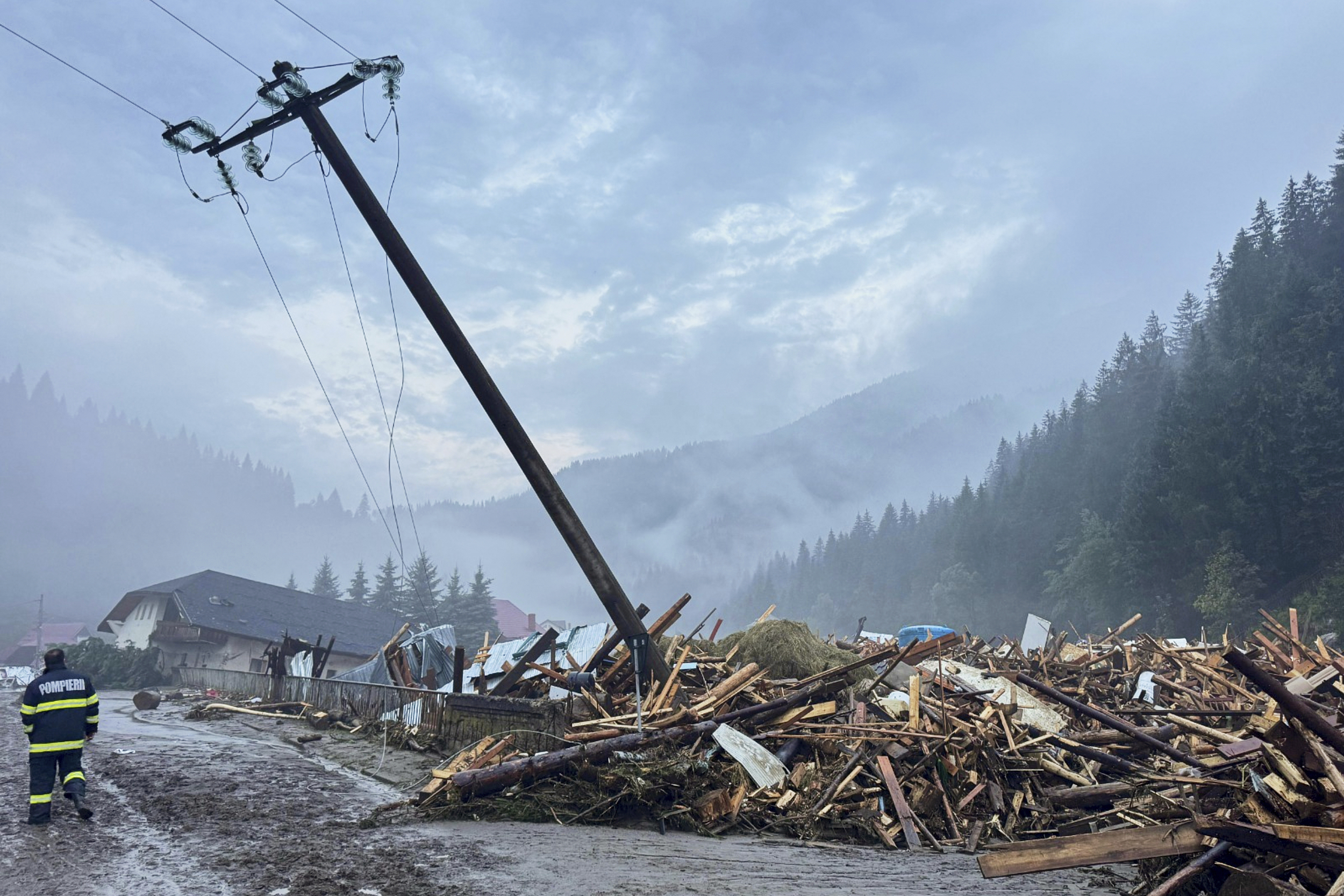 In this image released by the Romanian Emergency Services Suceava (ISU Suceava) first responders walk by damaged vehicles after a flash flood in the village of Brosteni, northern Romania, Monday, July 28, 2025. (Romanian Emergency Services - ISU Suceava via AP)