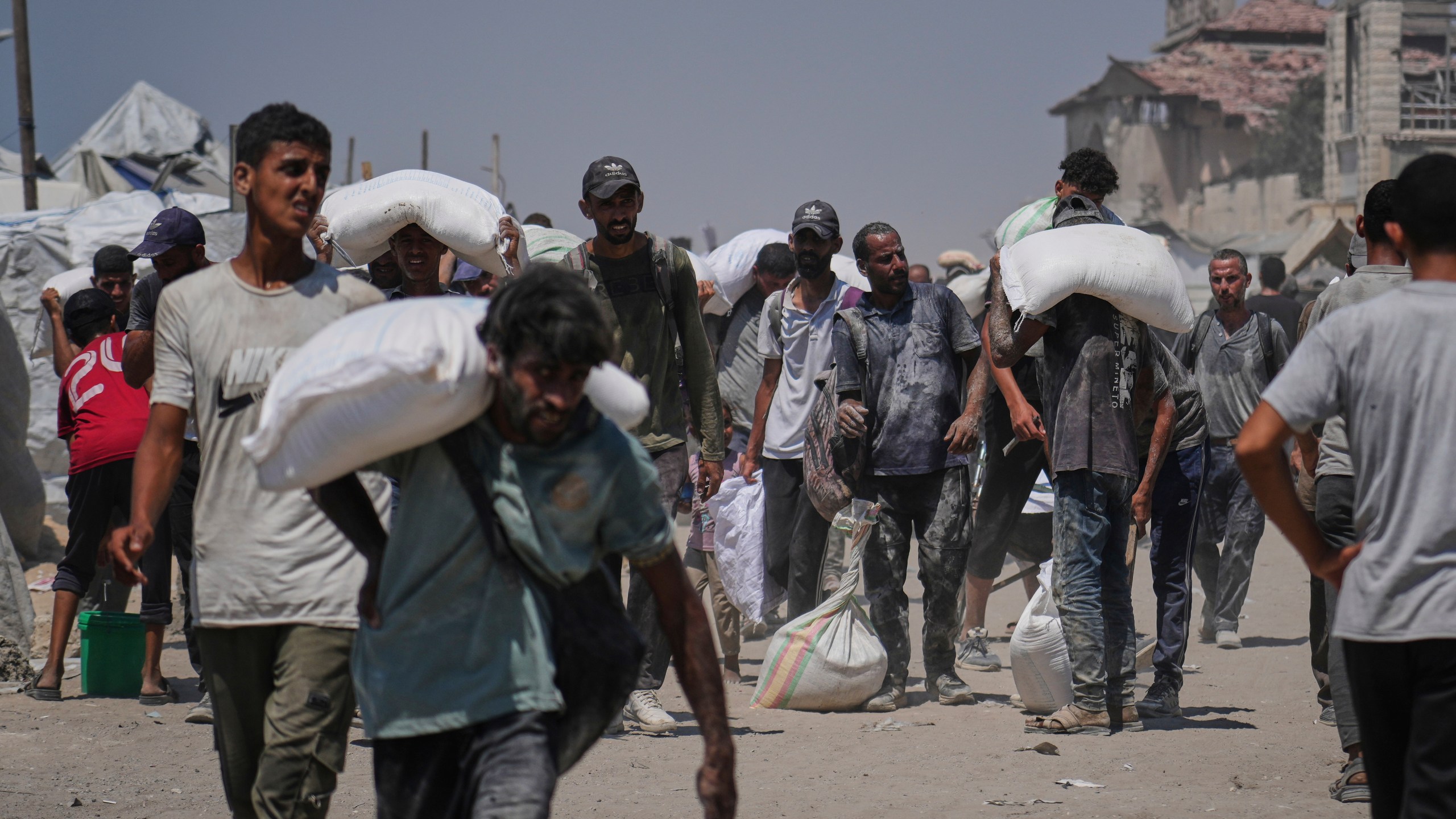 Palestinians carry sacks of flour unloaded from a humanitarian aid convoy that reached Gaza City from the northern Gaza Strip, Sunday, July 27, 2025. (AP Photo/Abdel Kareem Hana)