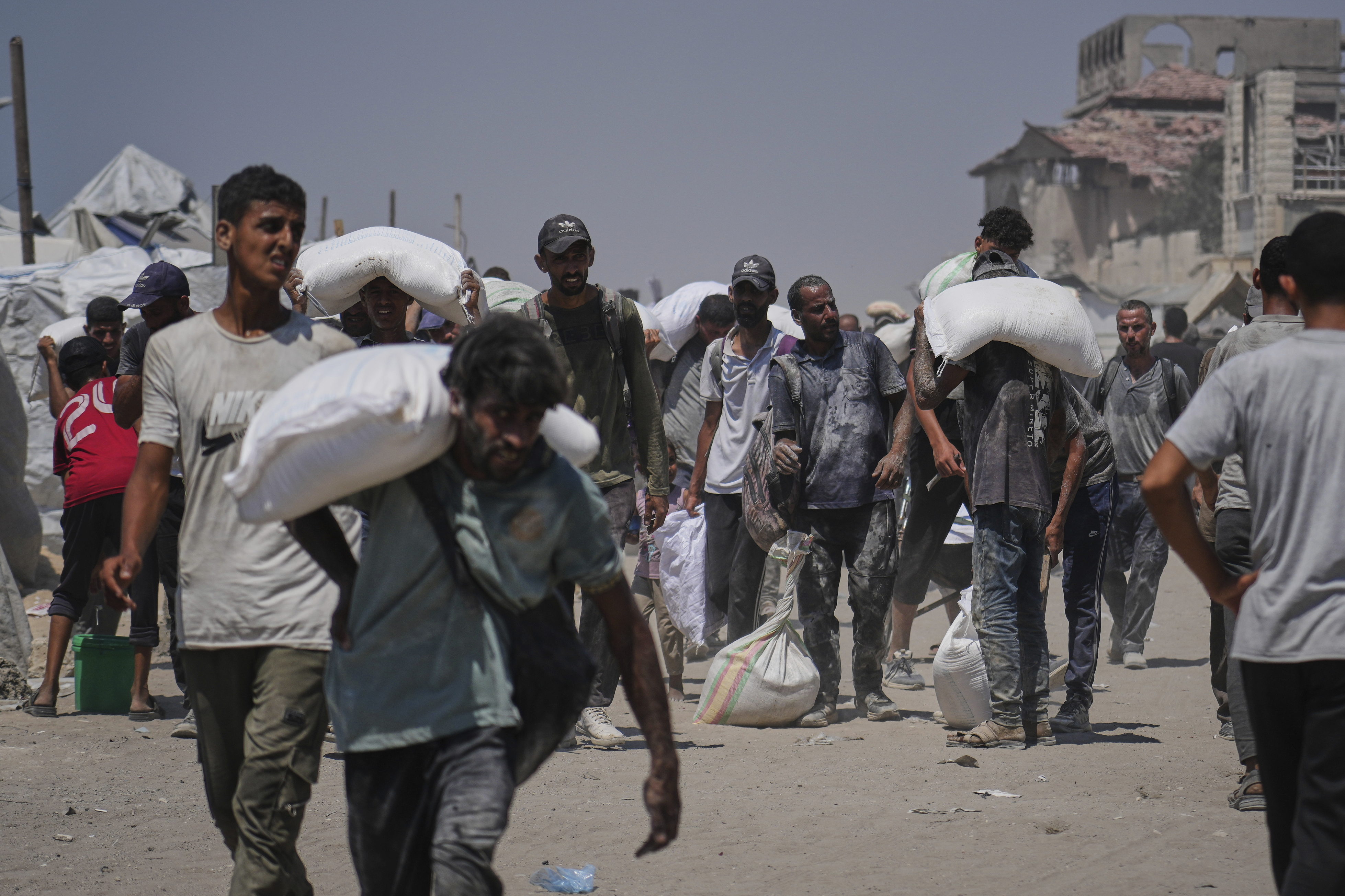 Palestinians carry sacks of flour unloaded from a humanitarian aid convoy that reached Gaza City from the northern Gaza Strip, Sunday, July 27, 2025. (AP Photo/Abdel Kareem Hana)