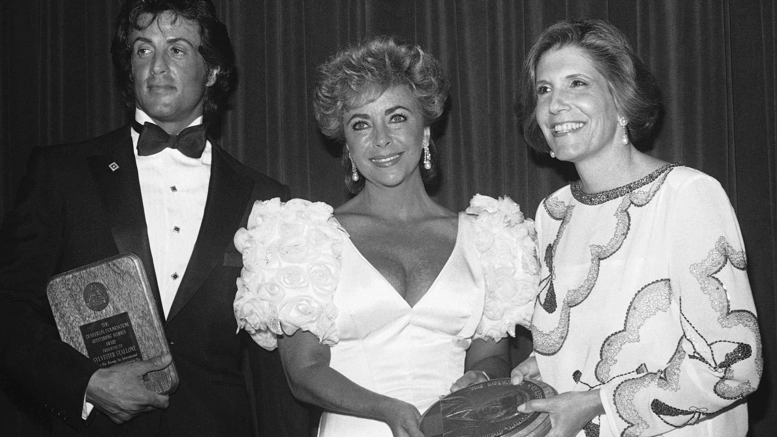 FILE - Wallis Annenberg, right, presents Elizabeth Taylor, center, and Sylvester Stallone with Devereux Foundation Awards at a ceremony, Thursday, July 12, 1984, Beverly Hills, Calif. (AP Photo/Nick Ut, file)