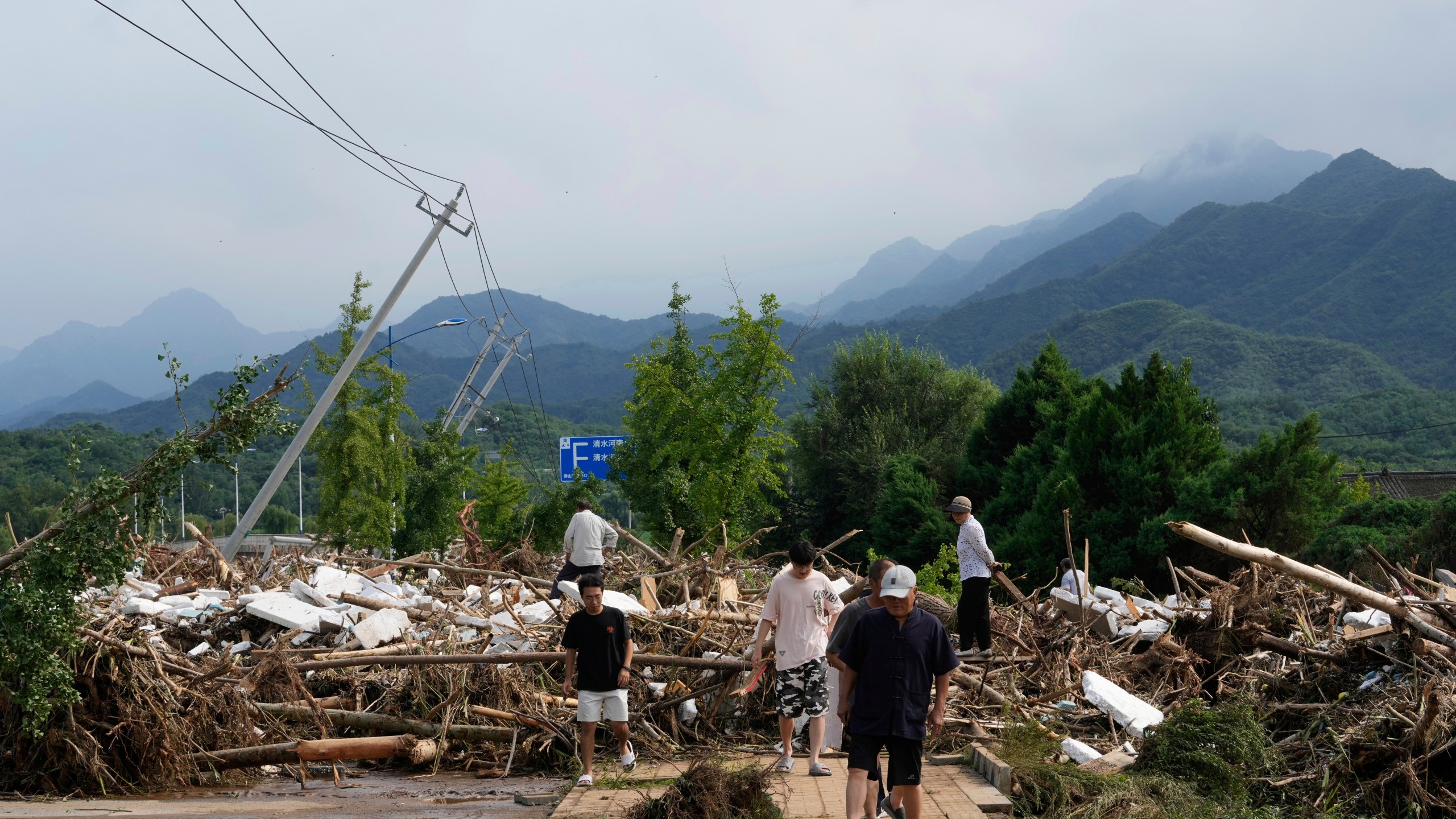 Local residents walks in front of a damaged road littered with broken tree branches after a heavy rains in Taishitun Town, Miyun district on the outskirts of Beijing, China, Monday, July 28, 2025. (AP Photo/Mahesh Kumar A.)