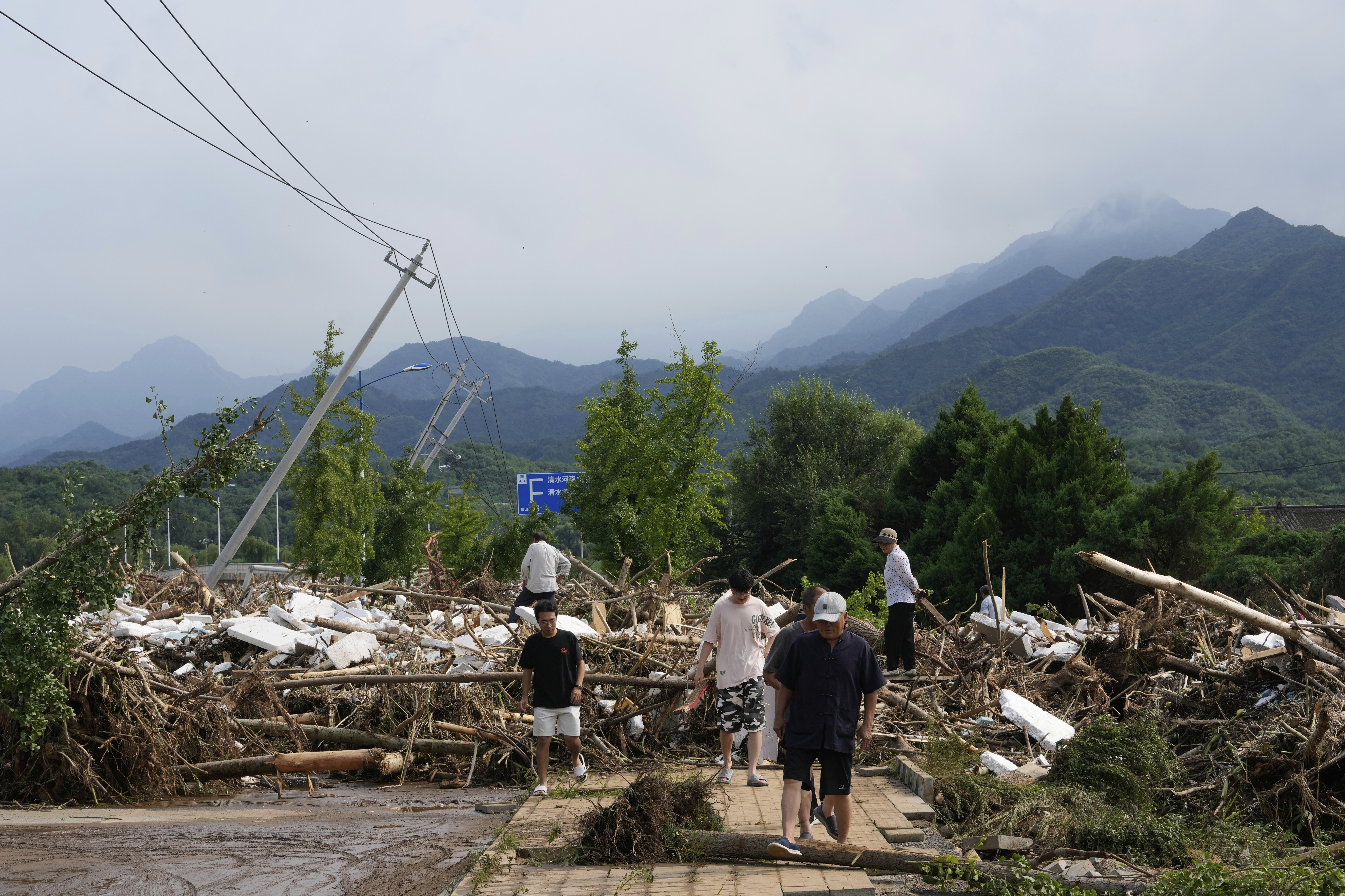 Local residents walks in front of a damaged road littered with broken tree branches after a heavy rains in Taishitun Town, Miyun district on the outskirts of Beijing, China, Monday, July 28, 2025. (AP Photo/Mahesh Kumar A.)
