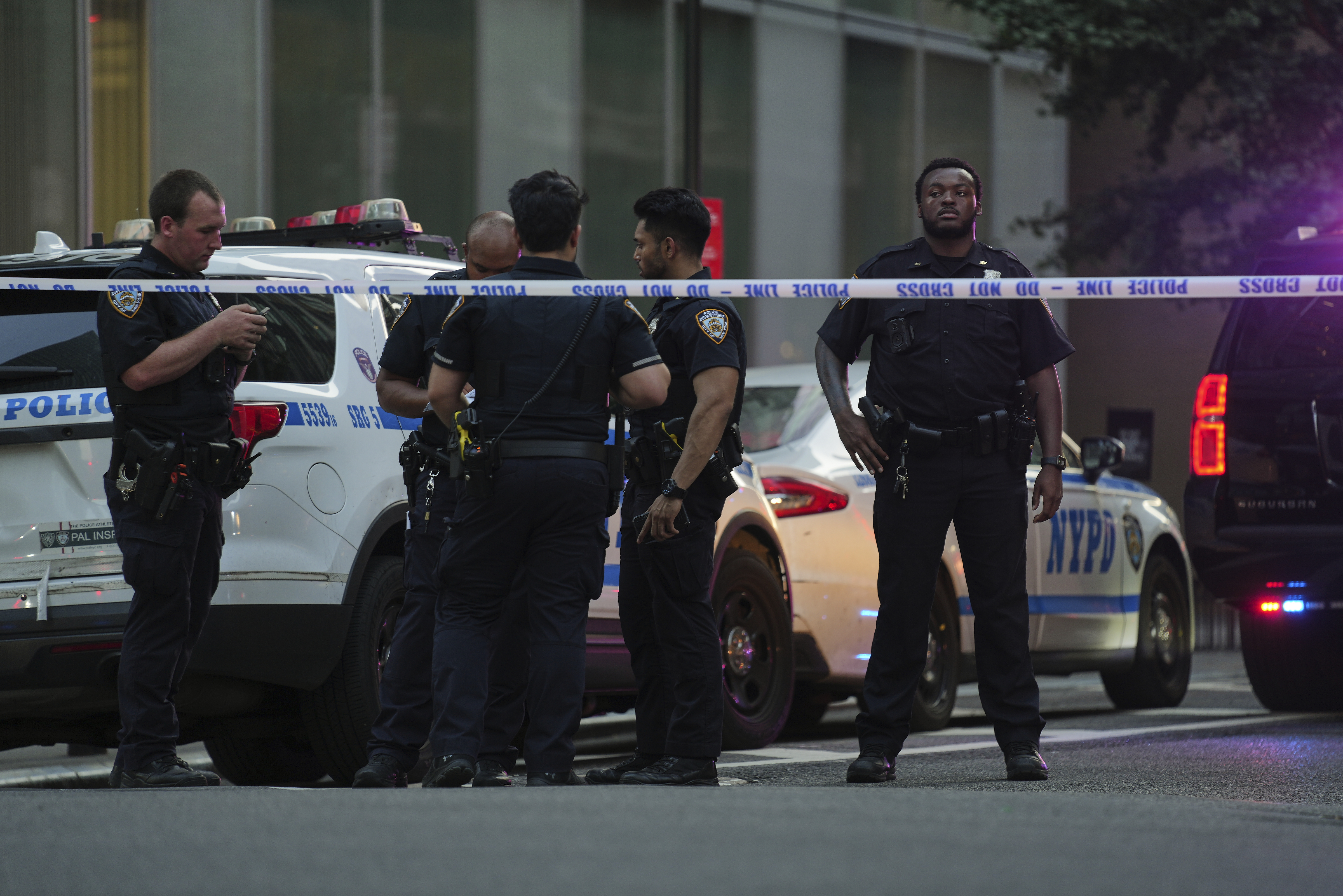 A New York Police officers gather at the scene on 52nd Street outside a Manhattan office building where two people were shot, including a New York police officer, Monday, July 28, 2025, in New York. (AP Photo/Angelina Katsanis)