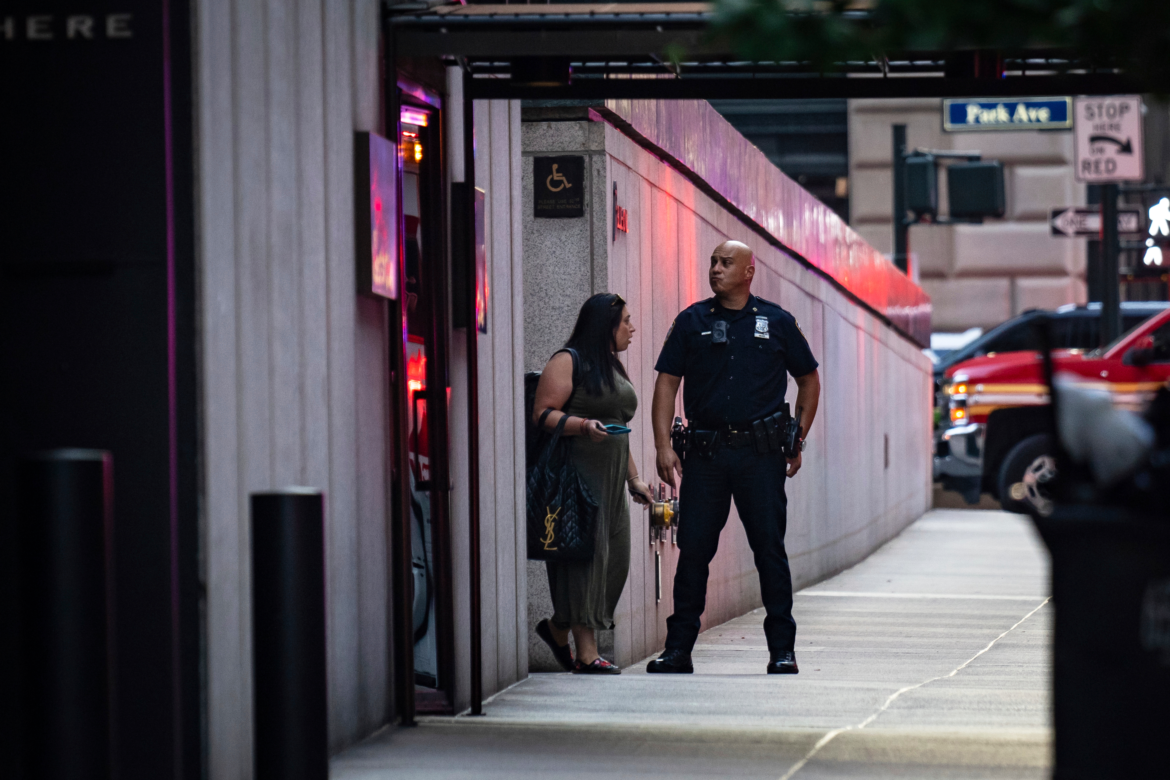 A New York police officer talks with a woman as she exits a Manhattan office building where two people were shot including a police officer, Monday, July 28, 2025, in New York. (AP Photo/Angelina Katsanis)