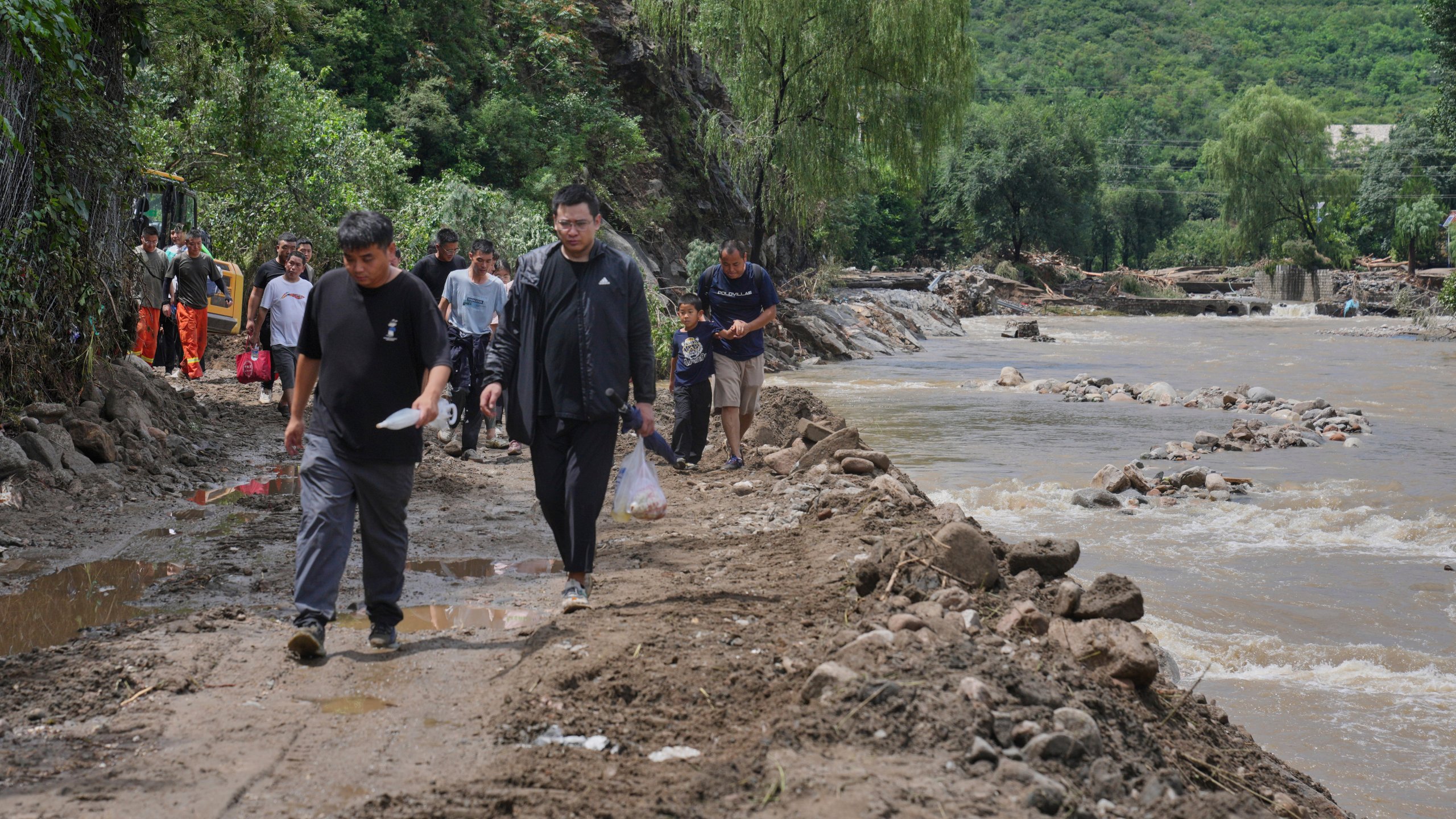 People walk on a road heading to Langjiayu village damaged by flood as they evacuate from the village after heavy rains in Miyun district on the outskirts of Beijing, Tuesday, July 29, 2025. (AP Photo/Andy Wong)