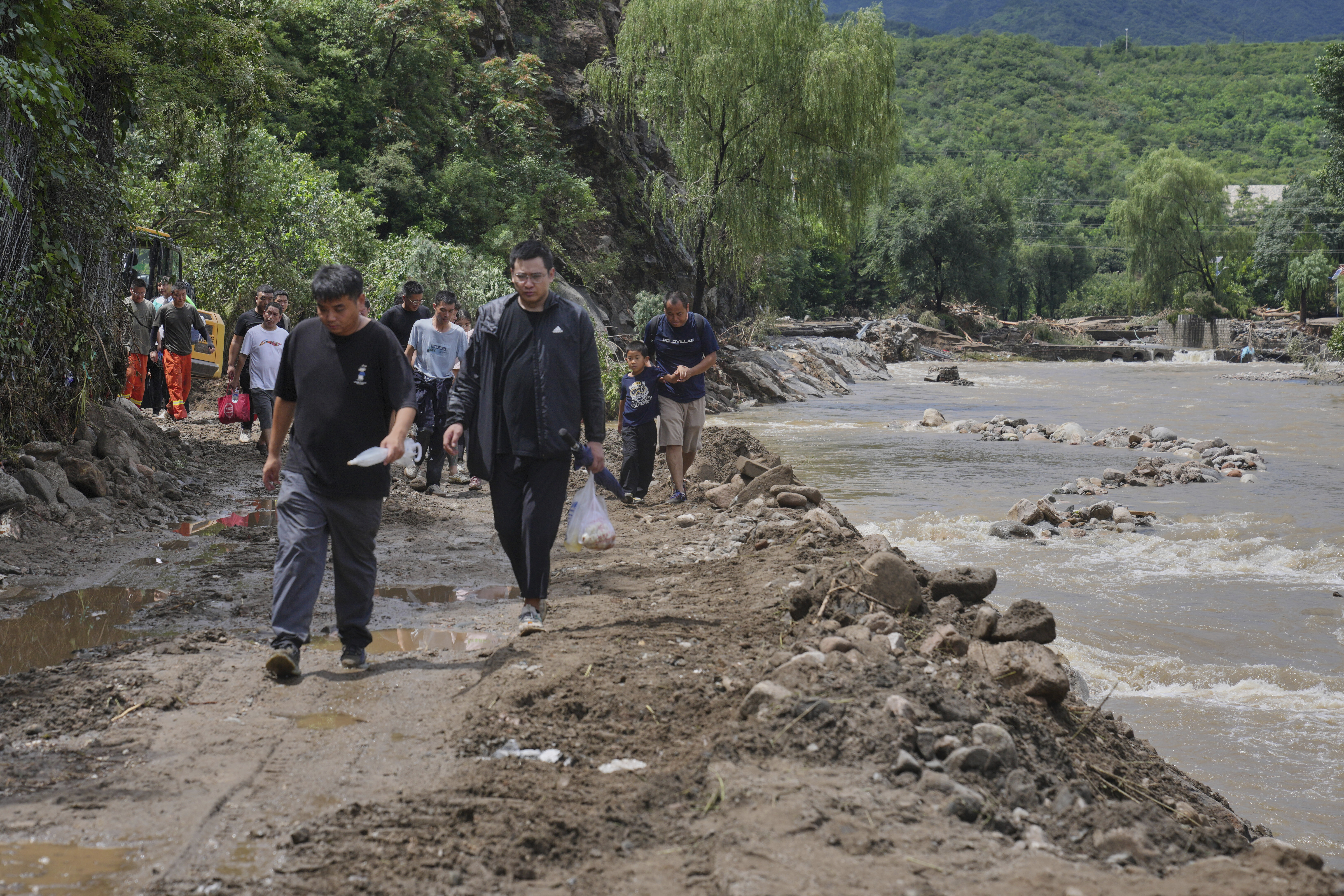 People walk on a road heading to Langjiayu village damaged by flood as they evacuate from the village after heavy rains in Miyun district on the outskirts of Beijing, Tuesday, July 29, 2025. (AP Photo/Andy Wong)