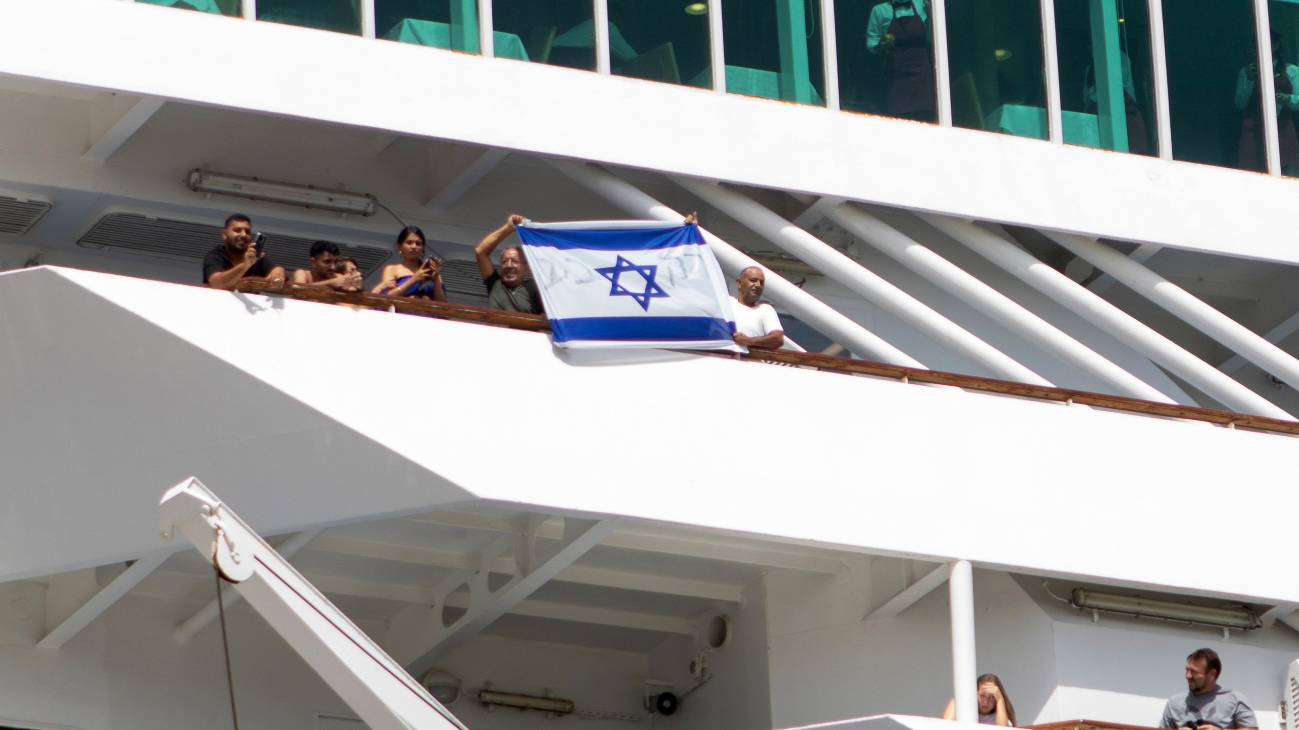 Two men hold up an Israeli flag during the departure of a cruise ship carrying Israeli tourists on the southeastern Aegean Sea island of Rhodes, Greece, Monday, July 28, 2025. (InTime News via AP)