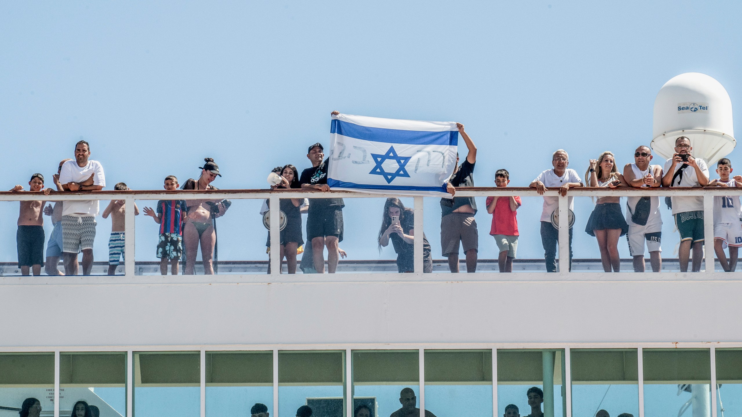 Israeli tourists hold the flag of their country as a cruise ship arrives at Agios Nikolaos port, on the island of Crete, Greece, Tuesday, July 29, 2025. (Antonis Zouridakis/Eurokinissi via AP)