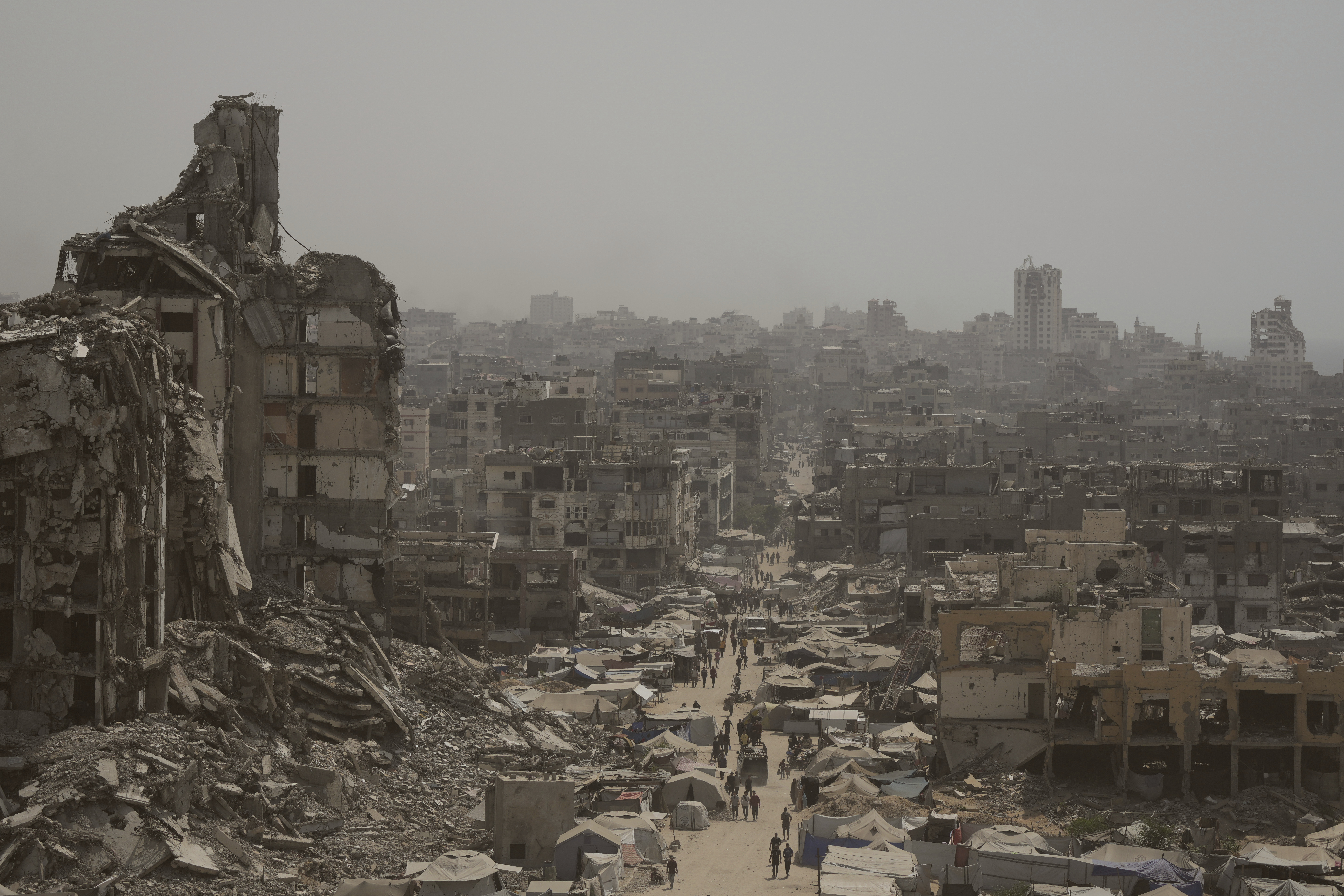 People walk along a street lined with destroyed buildings following Israeli bombardments during the Israel-Hamas war in the Gaza Strip, Tuesday, July 29, 2025. (AP Photo/Jehad Alshrafi)